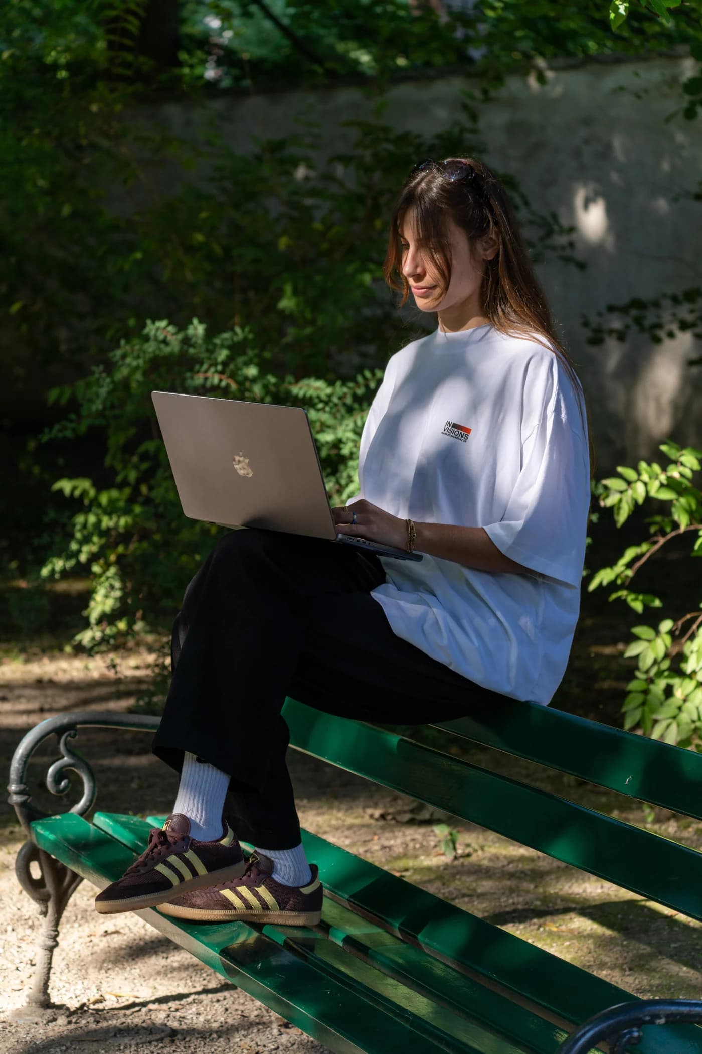 Person mit Invisions-Shirt sitzt mit dem Laptop auf einer Parkbank im Grünen.
