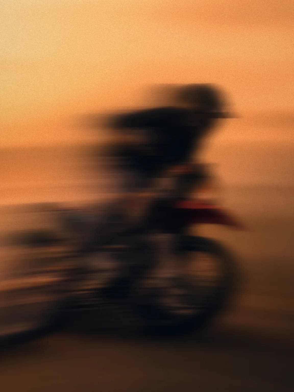 Mountainbike-Fahrt vor orangem Abendhimmel, stark in Bewegungsunschärfe