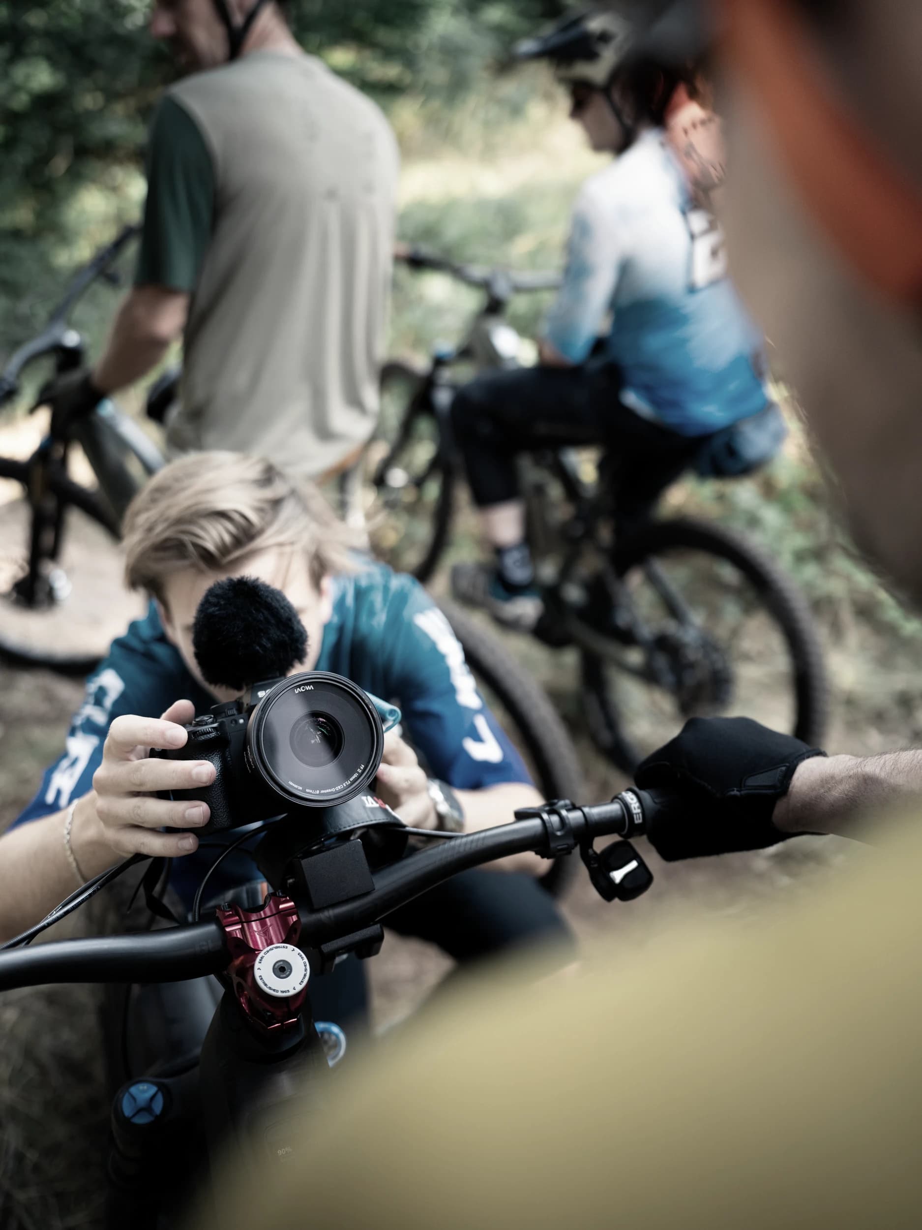 Kameramann der Werbeagentur Invisions filmt am Waldtrail, dahinter zwei Mountainbiker mit ihren Rädern.