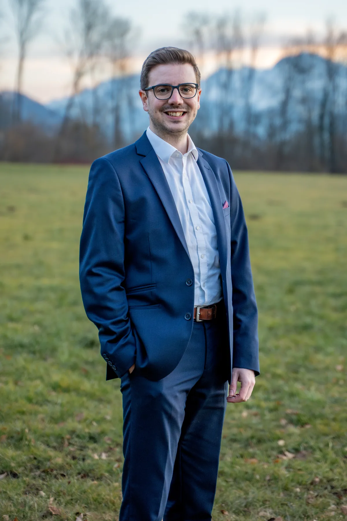 Florian Nachbagauer in ganzer Figur auf der Wiese vor den Bergen.