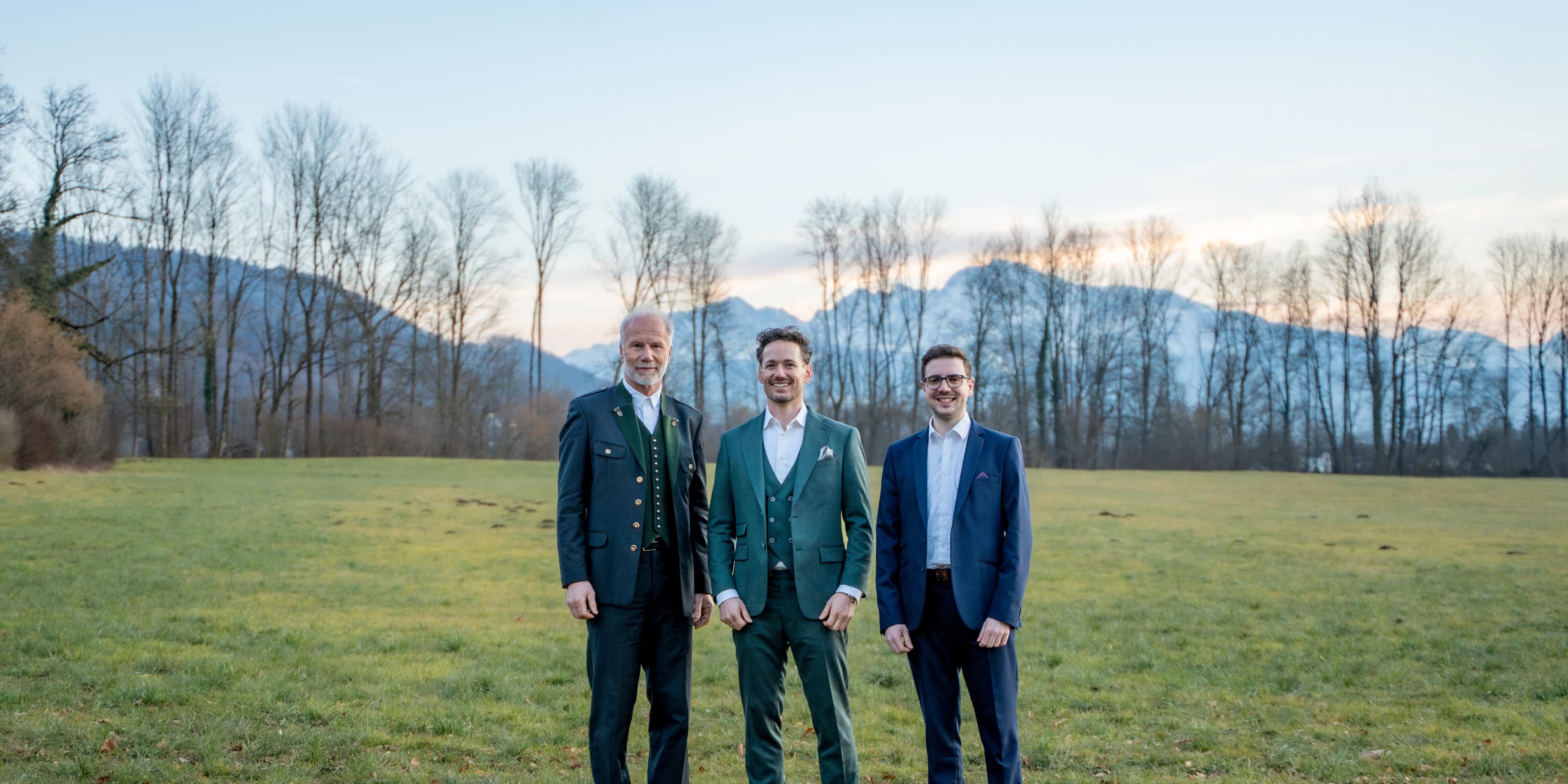 ActuQuant: Die drei Gründer stehen im Abendlicht auf einer Wiese, dahinter die Berge.