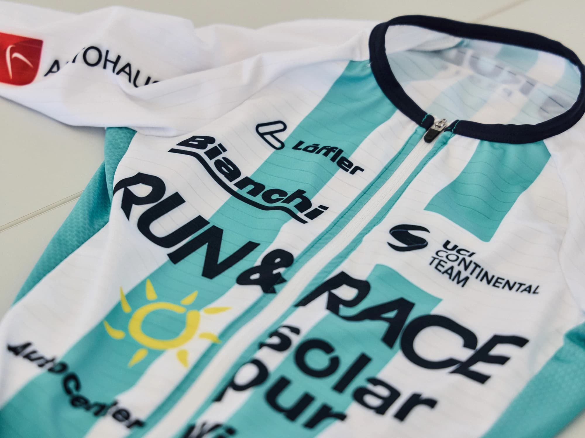 Nahaufnahme des fertigen Teamtrikots: weiße und türkise Streifen, darauf die Schriftzüge RUN & RACE solar pur, Bianchi und Löffler sowie der Hinweis UCI Continental Team.