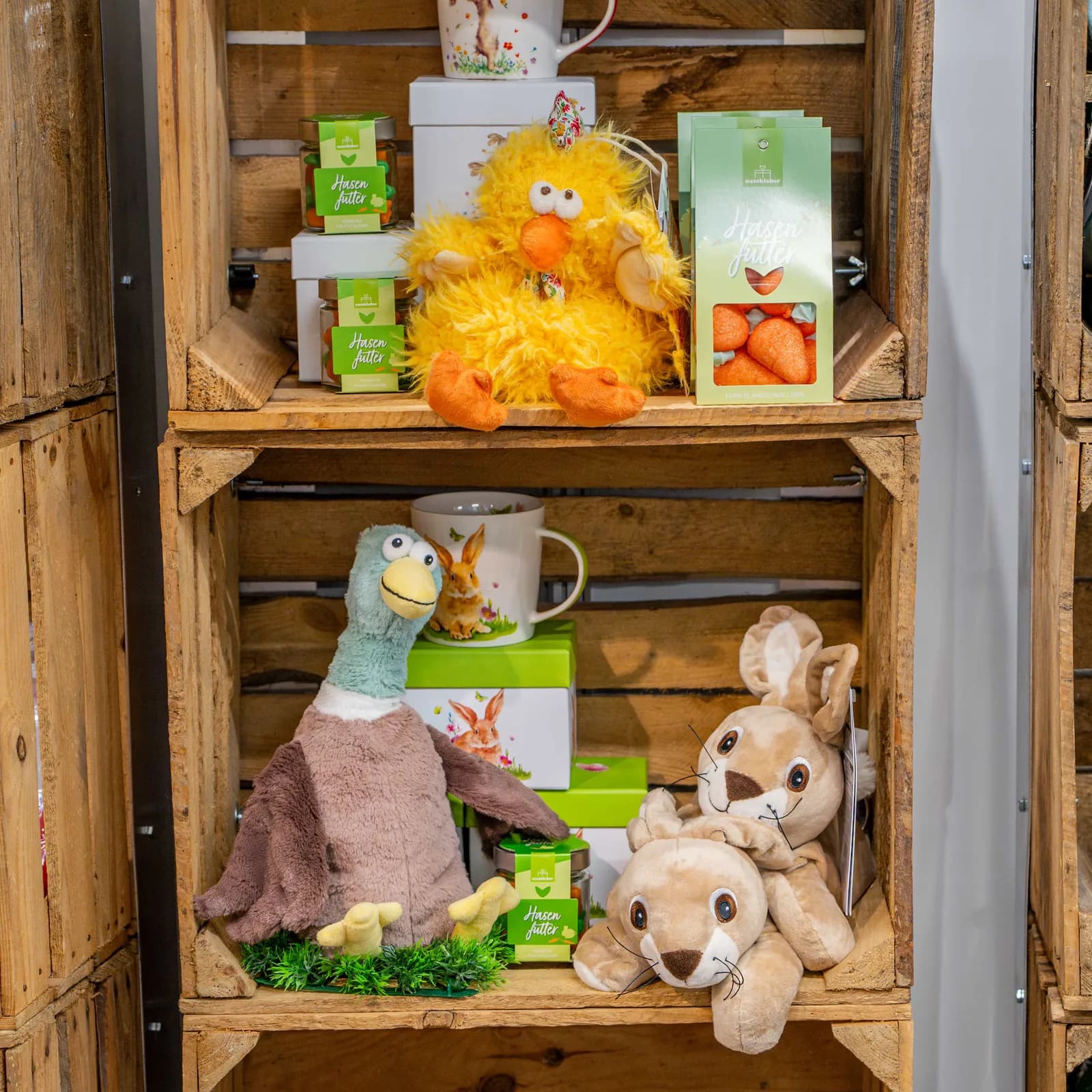 Eine Holzkiste am Messestand mit einer gelben Plüschente, Warmies-Tieren, einer Tasse und Produktschachteln.