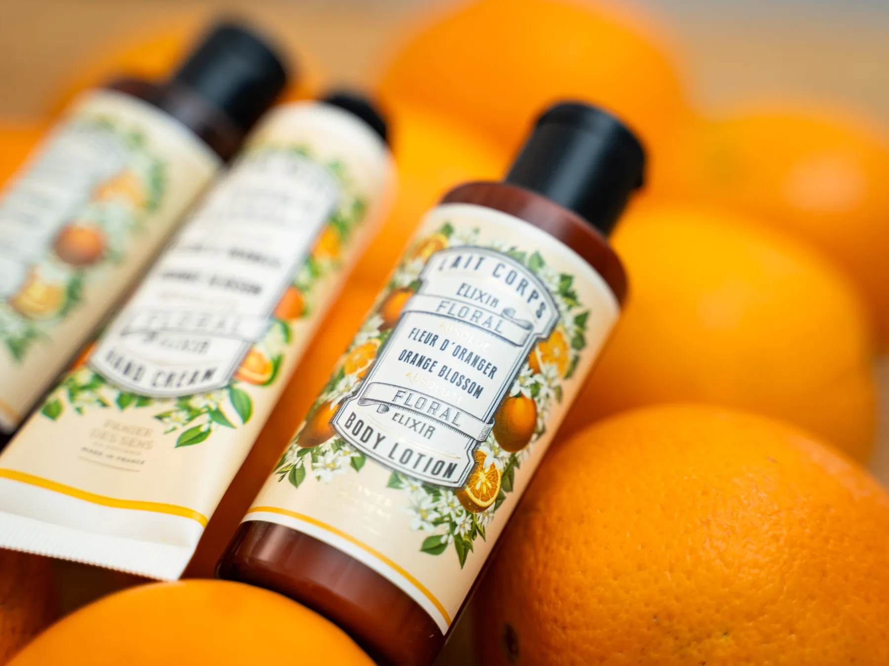 Drei Flaschen Body Lotion, Duschgel und Handcreme mit Orangenblütenetikett liegen zwischen frischen Orangen.