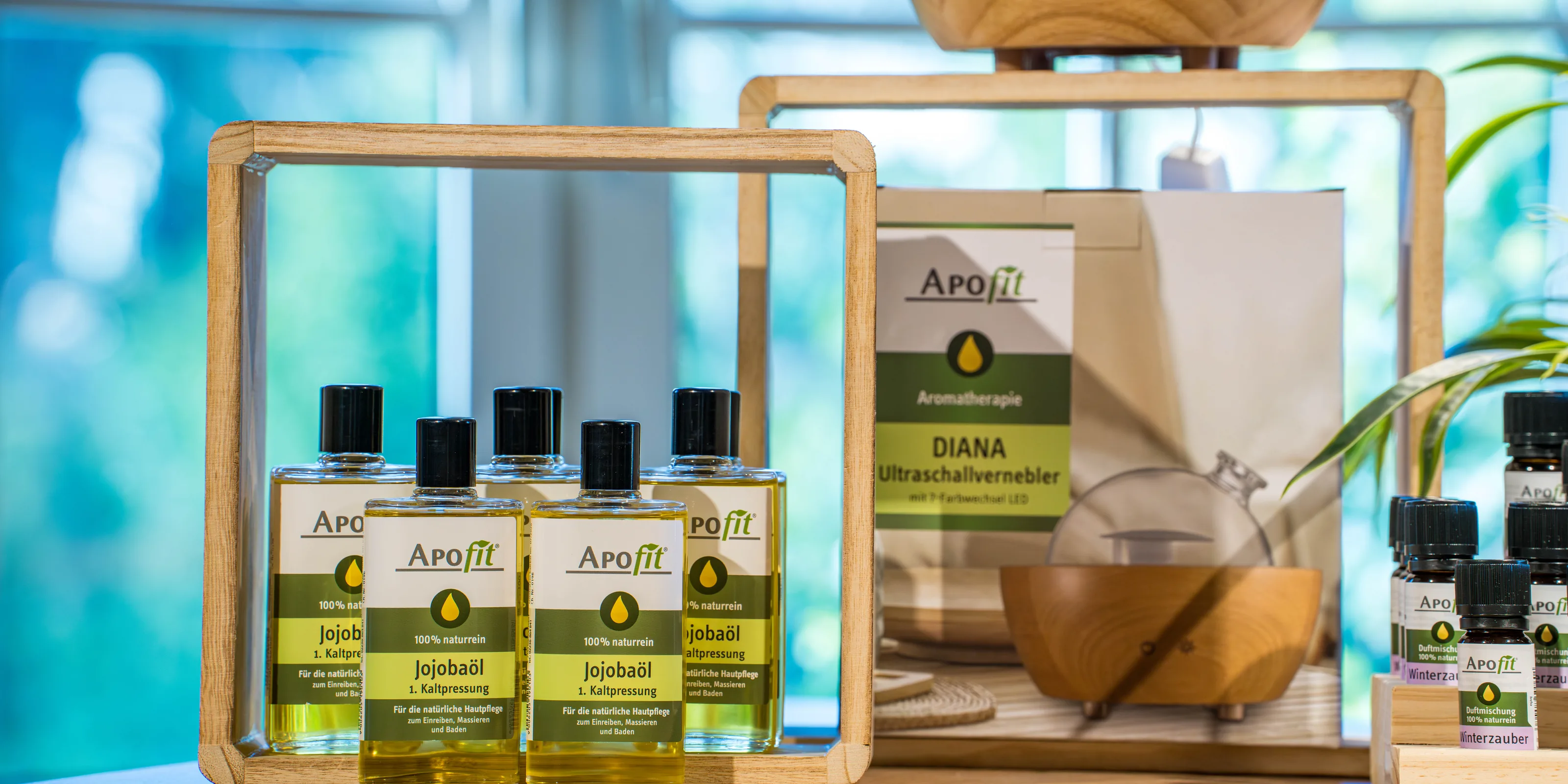 Grafik & Branding für APOfit: Flaschen mit den eigenen Etiketten in einem Holzrahmen, dahinter ein Werbeaufsteller für den Ultraschallvernebler.