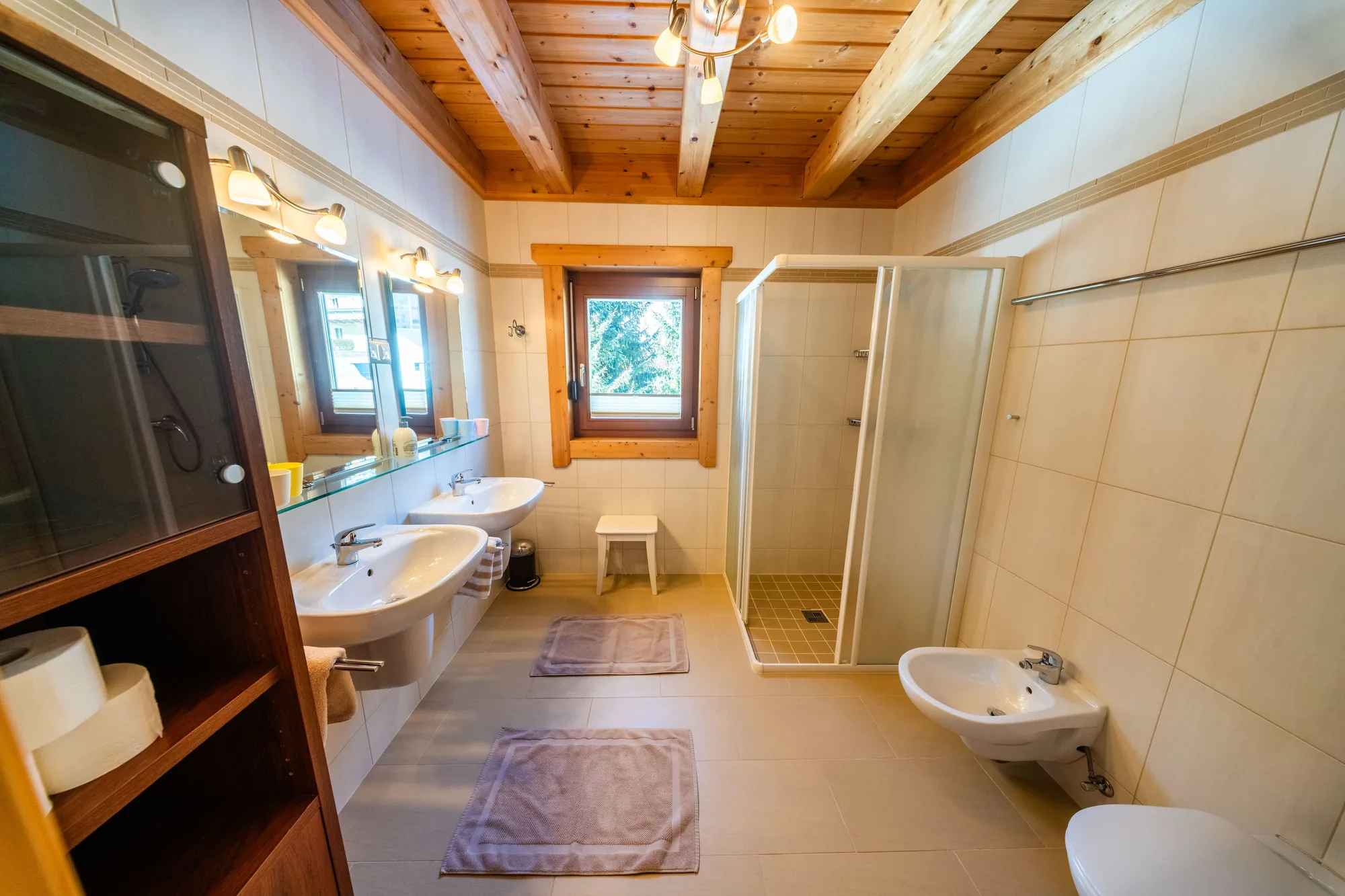 Eines der drei Bäder der Arlberg Kandahar Lodge: Doppelwaschtisch mit großem Spiegel, daneben eine bodengleiche Dusche hinter Glas.