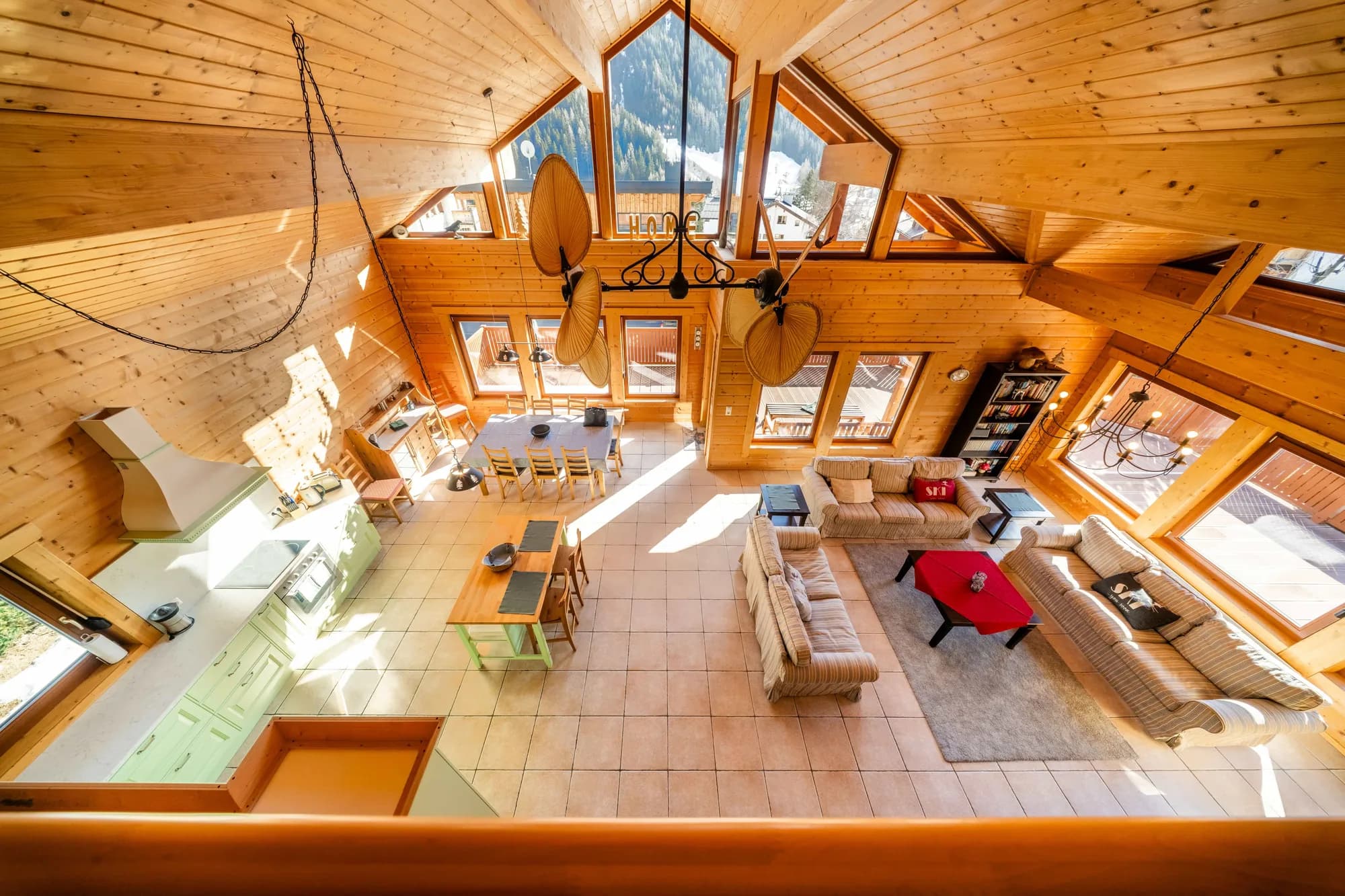 Der Wohnraum der Arlberg Kandahar Lodge von oben: der offene Holzgiebel über Sitzgruppe, Esstisch und Küche, an drei Seiten Fenster.