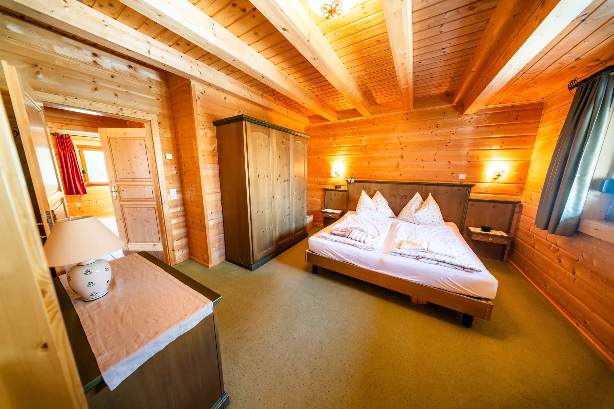 Das grüne Schlafzimmer der Arlberg Kandahar Lodge: Doppelbett mit hölzernem Kopfteil, Schrank und Schreibtisch an der Holzwand.
