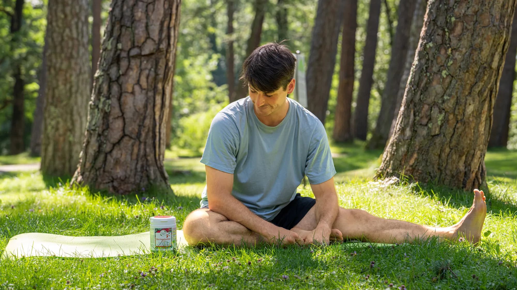 Ein junger Mann sitzt im Schneidersitz auf einer Matte im Park, neben ihm eine Dose Caesaro Med im Gras.