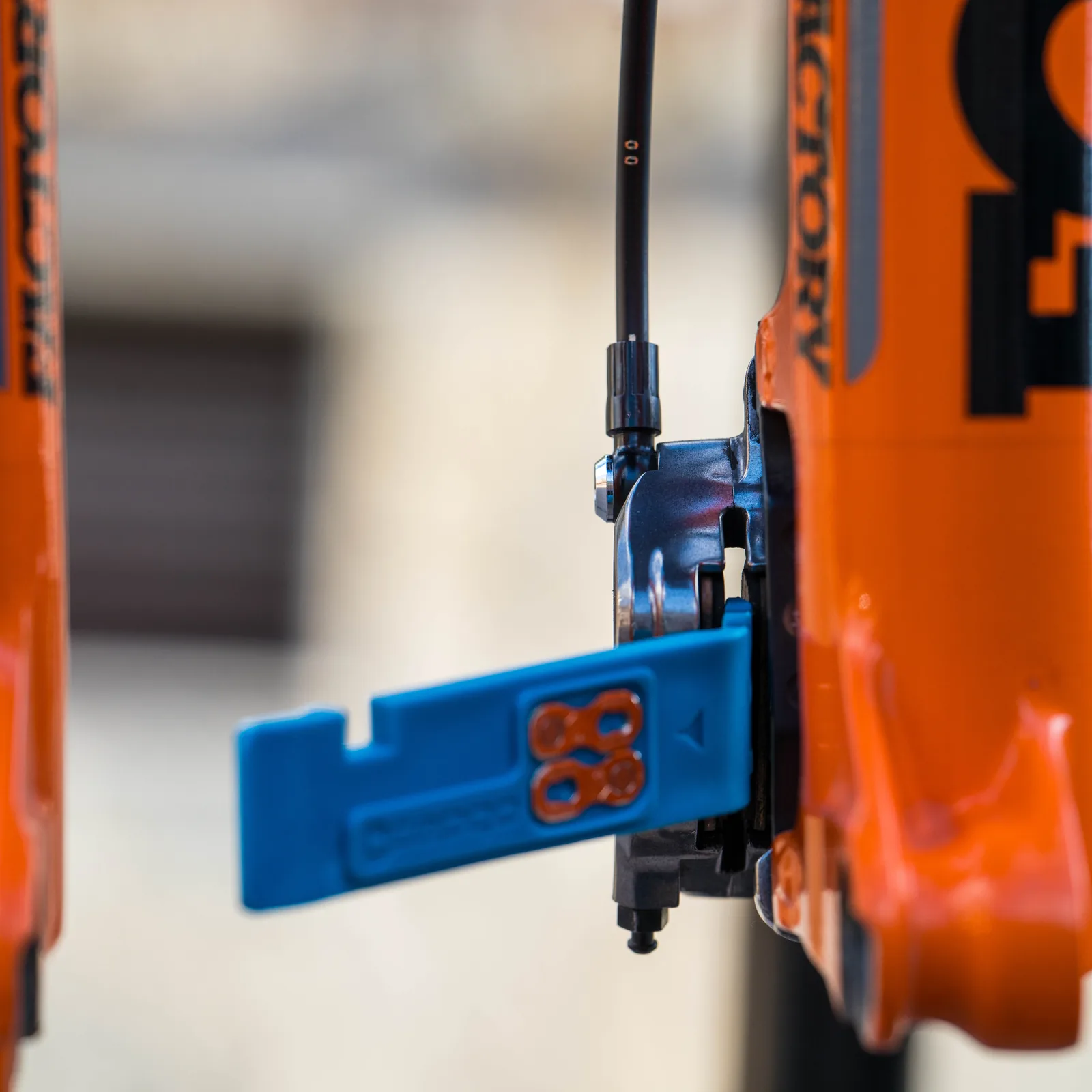 Das blaue Multitool von capgo steckt als Kolbenrücksteller im Bremssattel an einer orangen Federgabel.