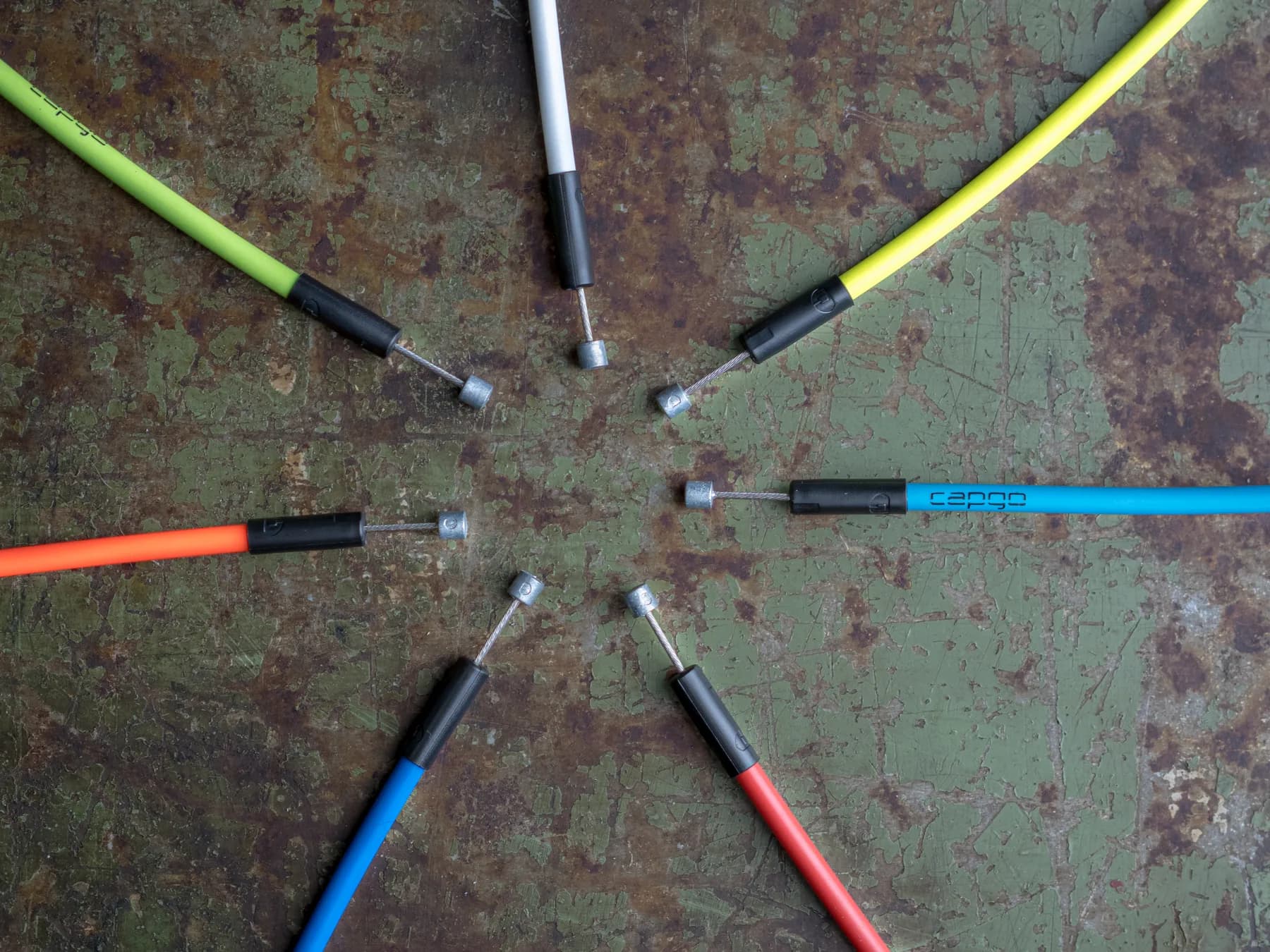 Sieben Züge in Neongrün, Gelb, Orange, Blau, Rot und Weiß zeigen mit ihren Endhülsen sternförmig zur Mitte einer rostigen Metallplatte.