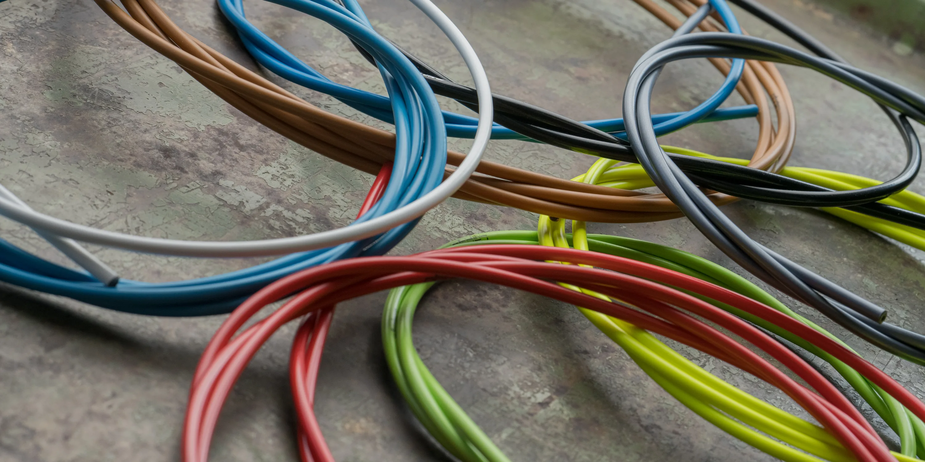 Außenhüllen für Schalt- und Bremszüge in Blau, Grau, Rot, Grün, Gelb und Braun liegen in Schlaufen übereinander auf einer rostigen Metallplatte.