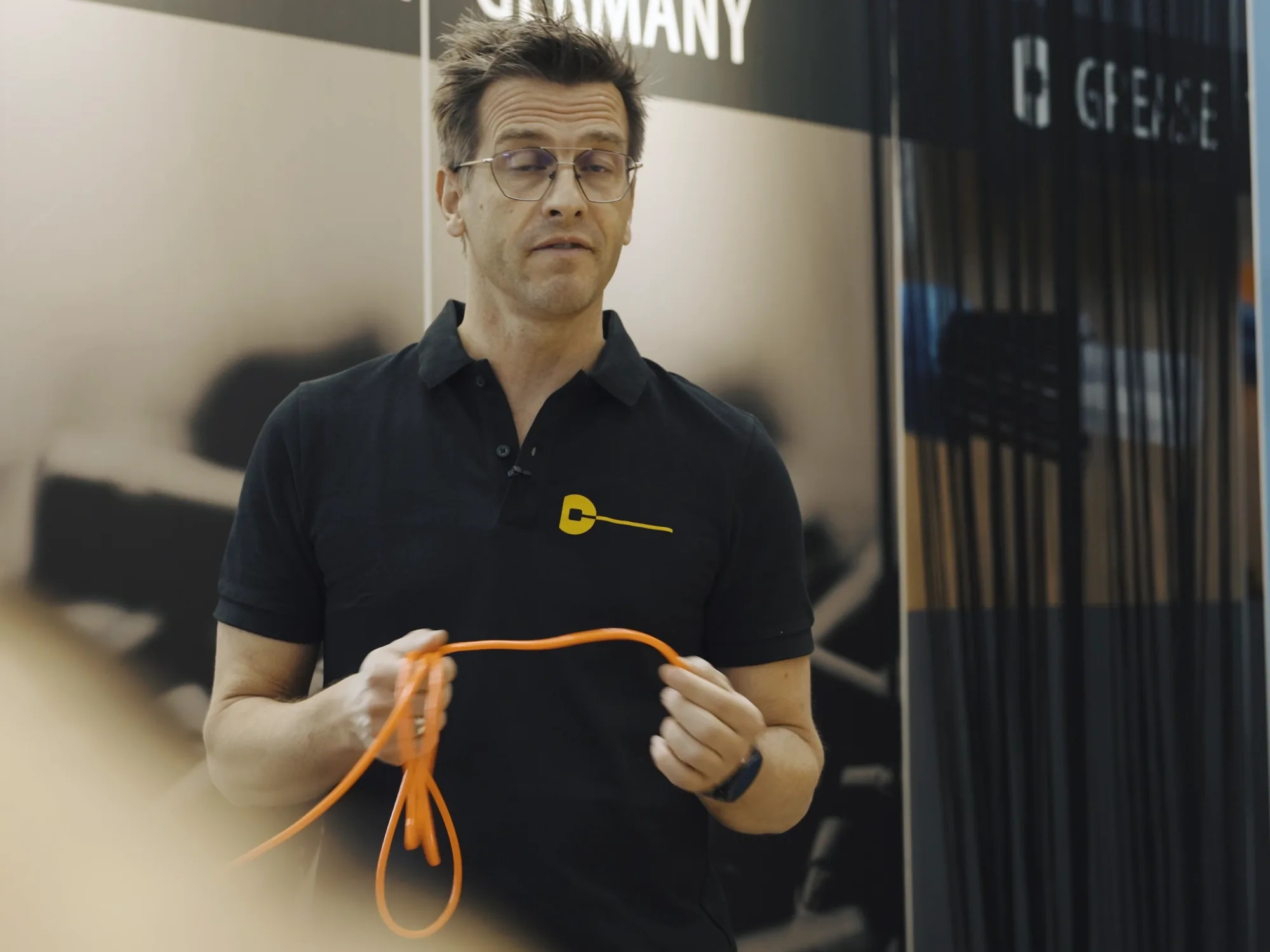 Ein Mann im schwarzen capgo-Polo hält am Messestand eine orange Außenhülle in beiden Händen und erklärt sie in die Kamera, Standbild aus dem Eurobike-Film 2022.