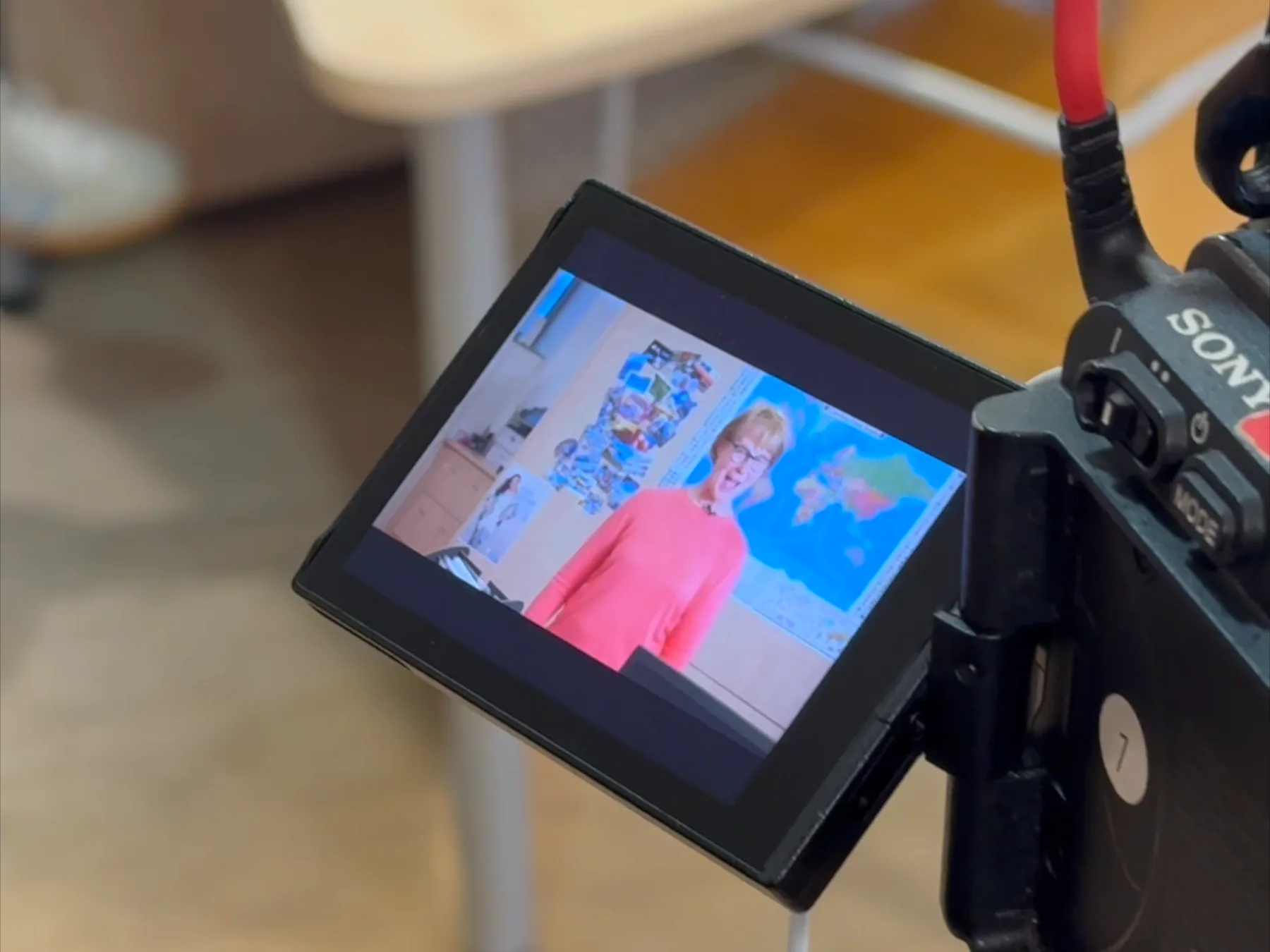 Der aufgeklappte Monitor einer Sony-Kamera zeigt eine Beraterin im roten Pullover vor der Katalogwand, das Gehäuse der Kamera daneben unscharf.