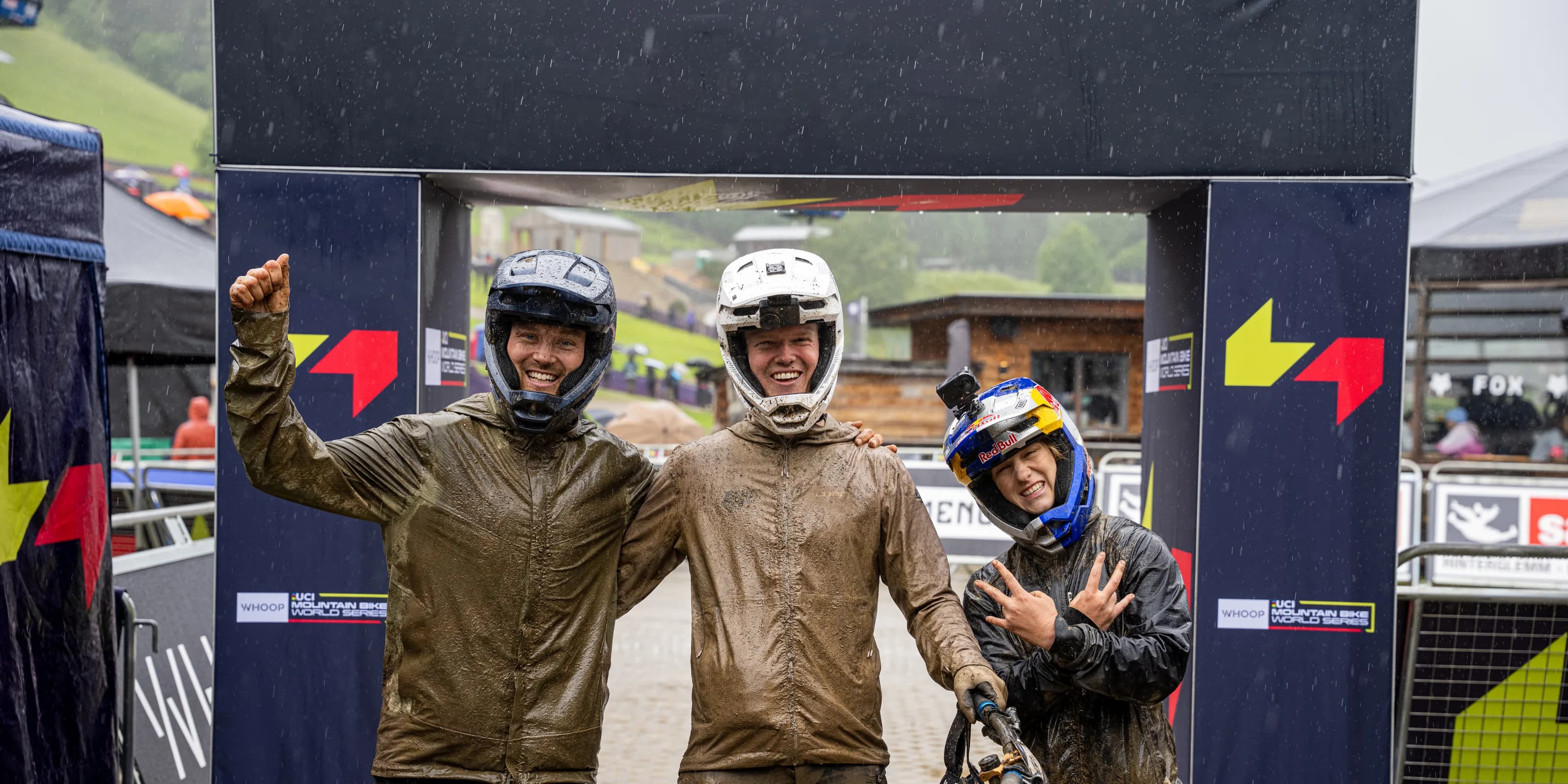 CUBE Actionteam: Drei Fahrerinnen und Fahrer stehen von Kopf bis Fuss im Schlamm unter dem Zielbogen eines Weltcuplaufs in Leogang und lachen in die Kamera.