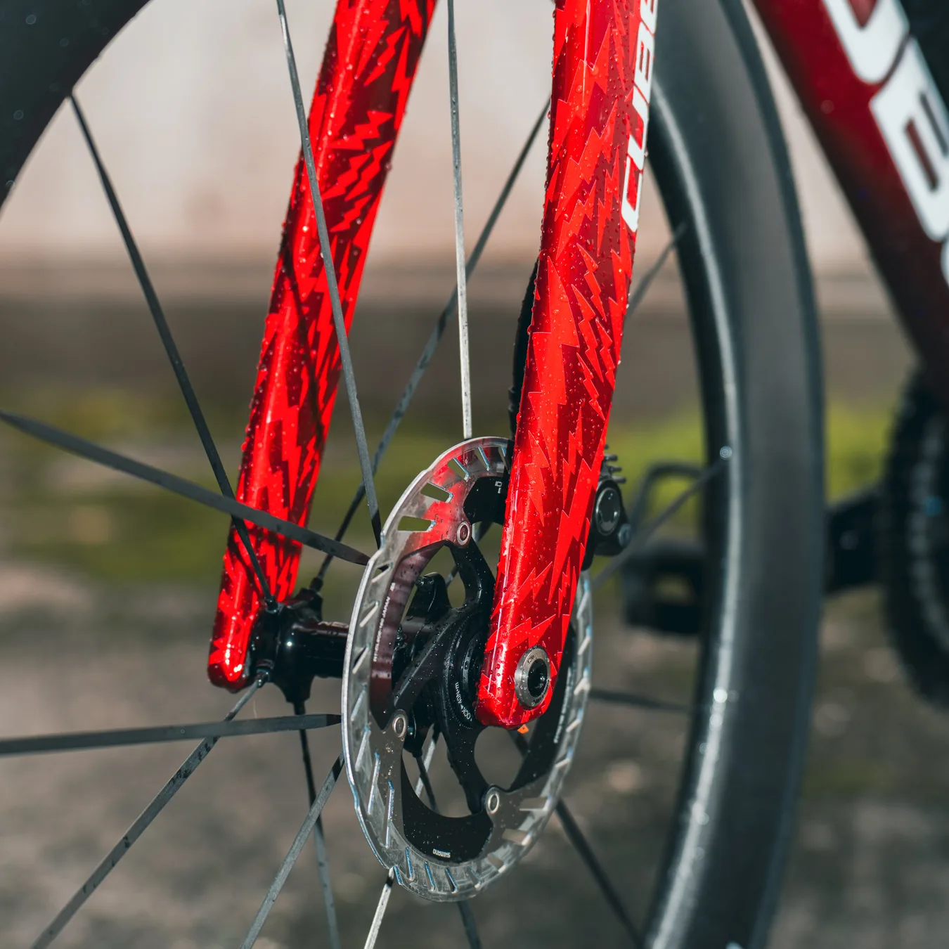 Die rote Gabel des Litening Aero mit Blitzgrafik von nahem, dahinter die Bremsscheibe und das Vorderrad auf nassem Asphalt.