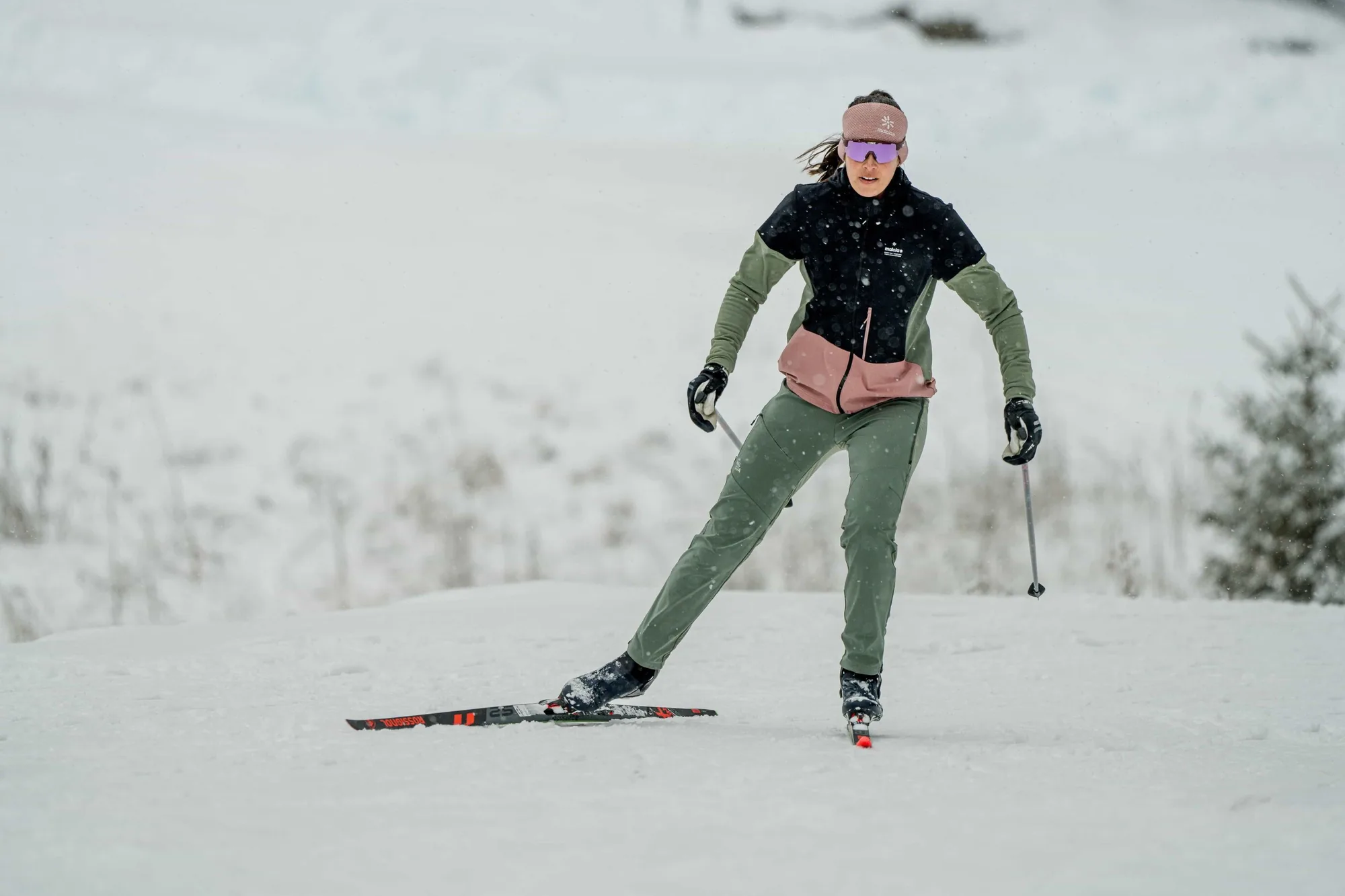 Eine einzelne Langläuferin skatet über eine weite, leere Schneefläche, viel freier Schnee über und neben ihr.