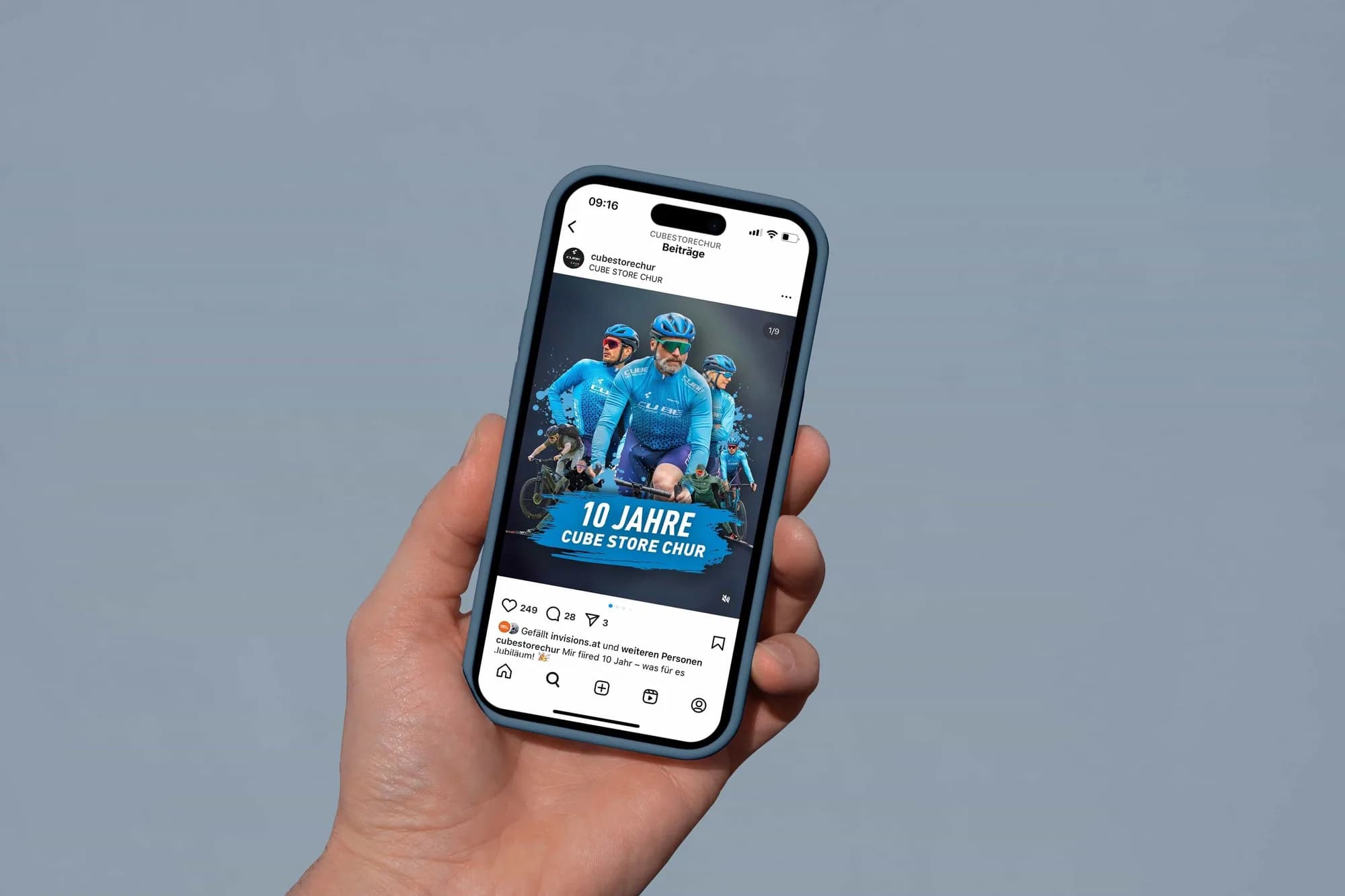Eine Hand hält ein iPhone vor blaugrauem Grund, auf dem Display ein Instagram-Beitrag des Kontos cubestorechur mit demselben Jubiläumsmotiv wie das Plakat.
