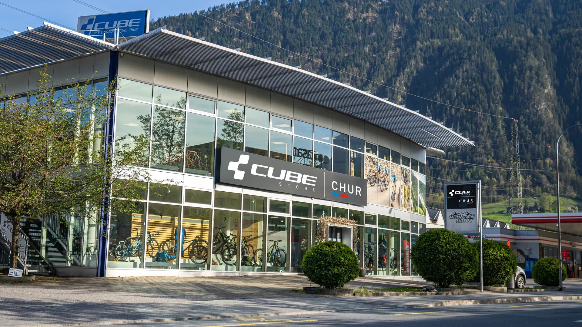 Der CUBE STORE CHUR an der Rossbodenstrasse in Chur: ein Glasbau mit dem Schriftzug CUBE Store Chur, dahinter der bewaldete Hang.