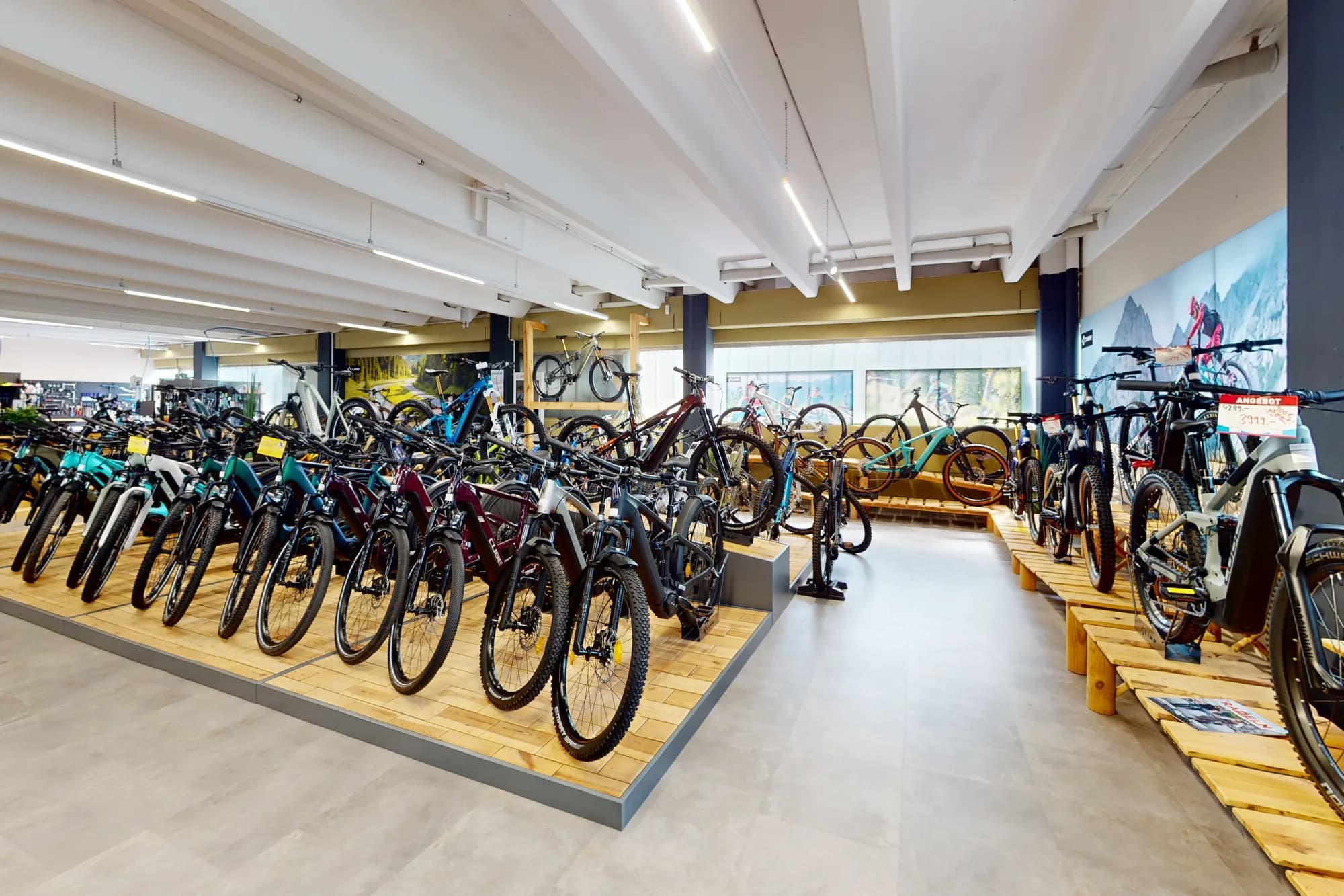 Die E-Bike-Fläche im CUBE Store Deggendorf: mehrere Reihen Räder auf hellen Holzpodesten, dahinter die Zubehörwand und die Fensterfront.