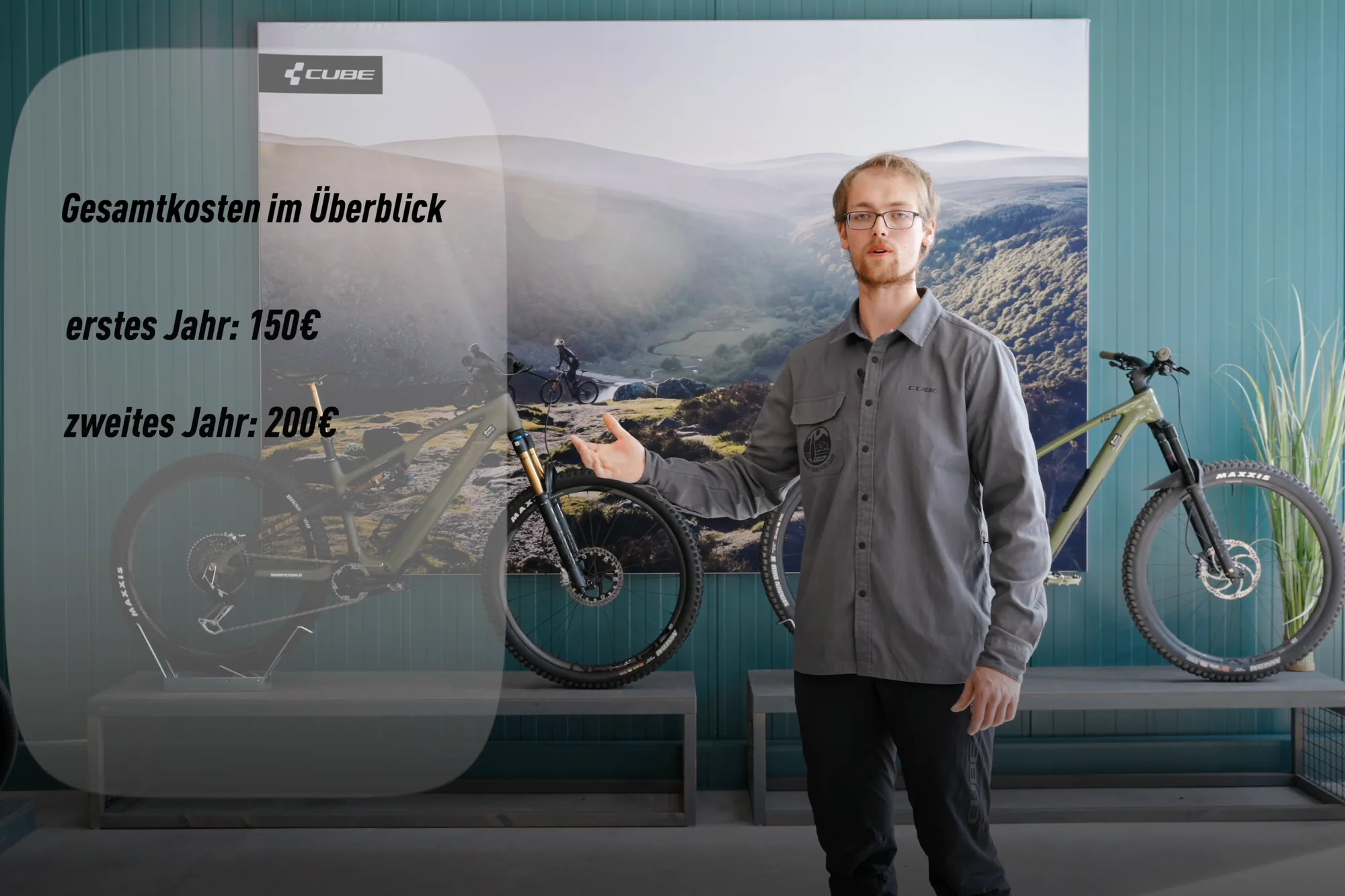 Standbild aus dem Film über Reparaturkosten: eine eingeblendete Karte mit der Überschrift Gesamtkosten im Überblick, daneben der Mitarbeiter vor zwei Mountainbikes.