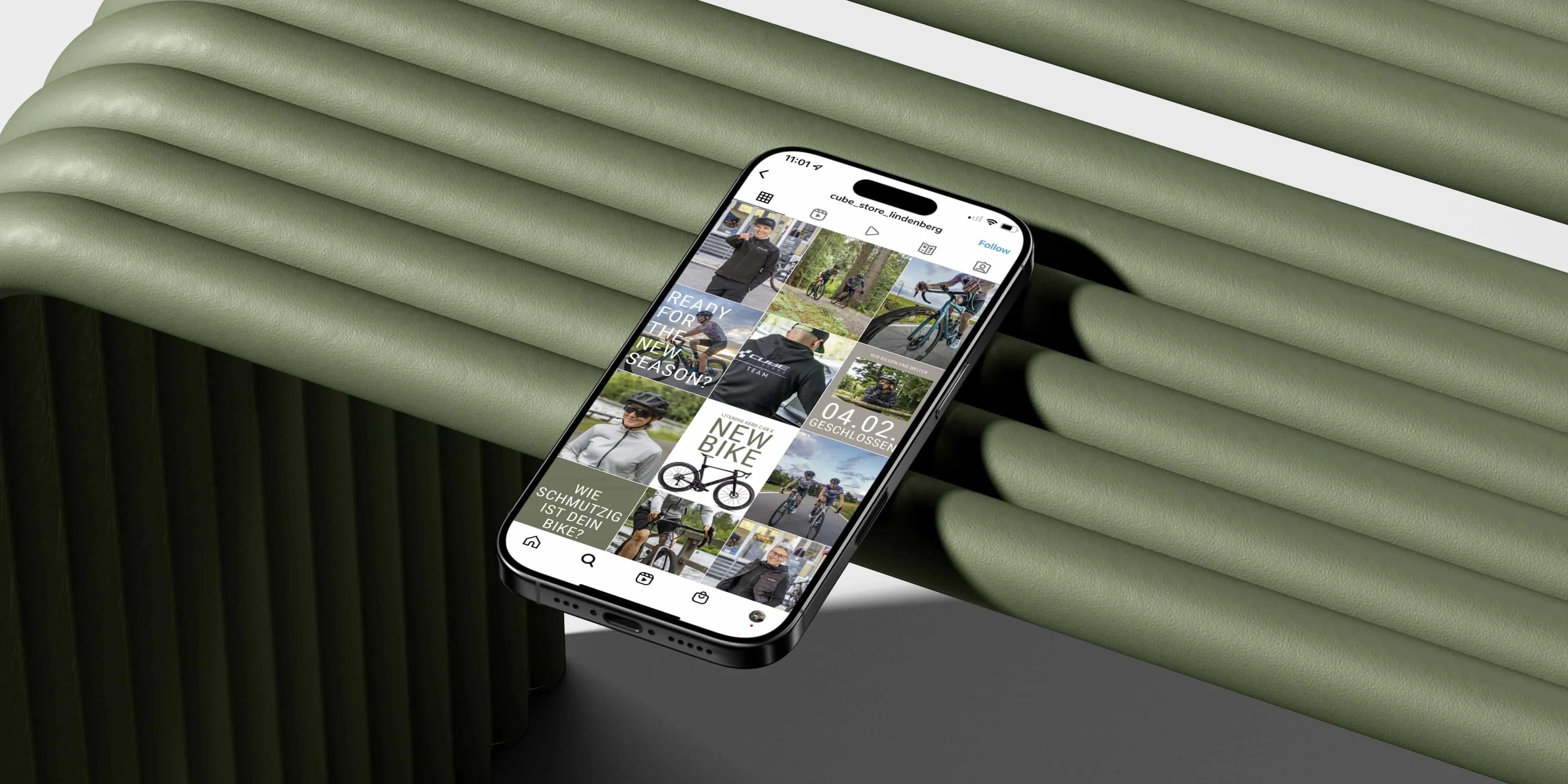 CUBE Store Lindenberg: Ein Telefon auf einer salbeigrünen Bank zeigt das Instagram-Profil des Stores mit dem gestalteten Beitragsraster.