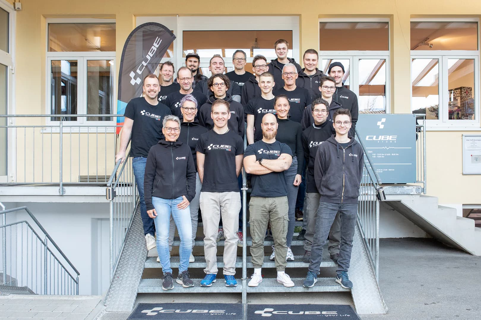 Das Team des CUBE Store Lindenberg auf der Treppe vor dem Eingang, rund zwanzig Personen in schwarzen CUBE-Shirts.