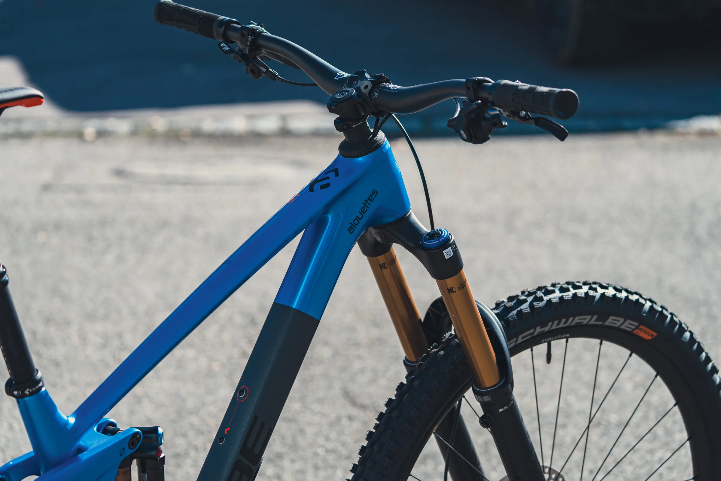 Nahaufnahme eines blauen CUBE Mountainbikes vor dem Laden: Cockpit, Steuerrohr und die goldene Federgabel im Sonnenlicht.