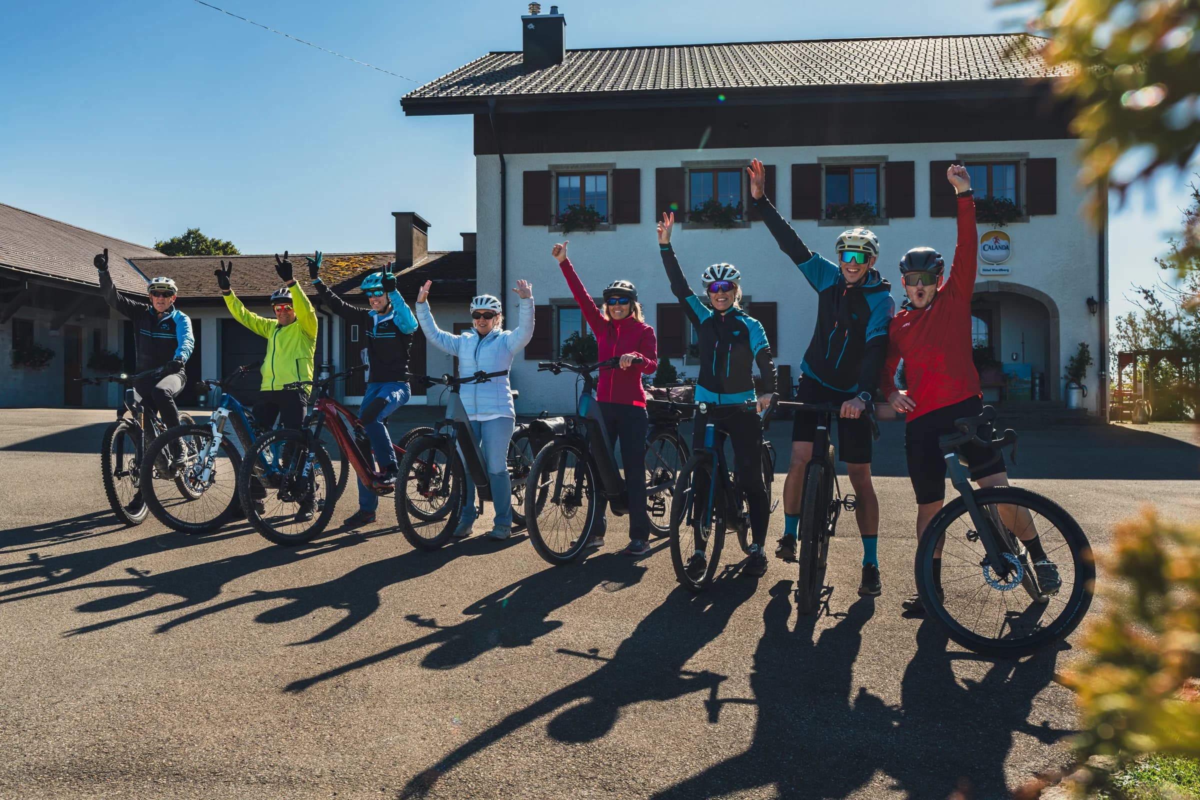 Eine Gruppe Radfahrer steht mit ihren Rädern vor einem Haus und winkt in die Kamera.