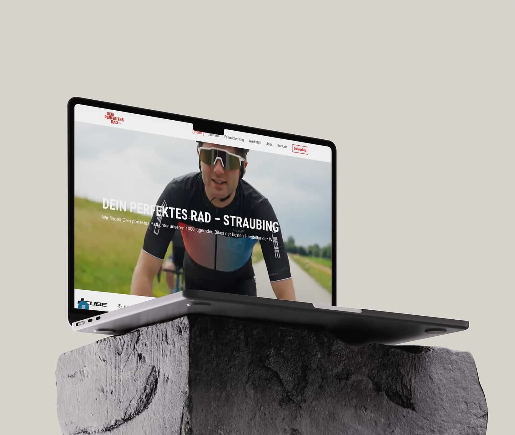 Ein MacBook auf einem Findling zeigt die Startseite von Dein perfektes Rad Straubing mit einem Rennradfahrer im Hero.
