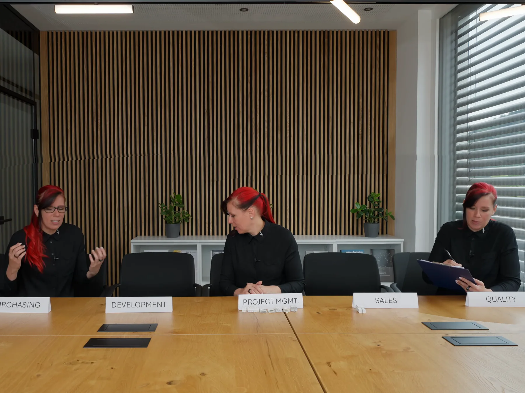 Dieselbe Frau mit roten Haaren sitzt dreimal an einem langen Besprechungstisch, vor den Schildern Development, Project Mgmt. und Quality, Standbild aus Folge 3 der Serie.