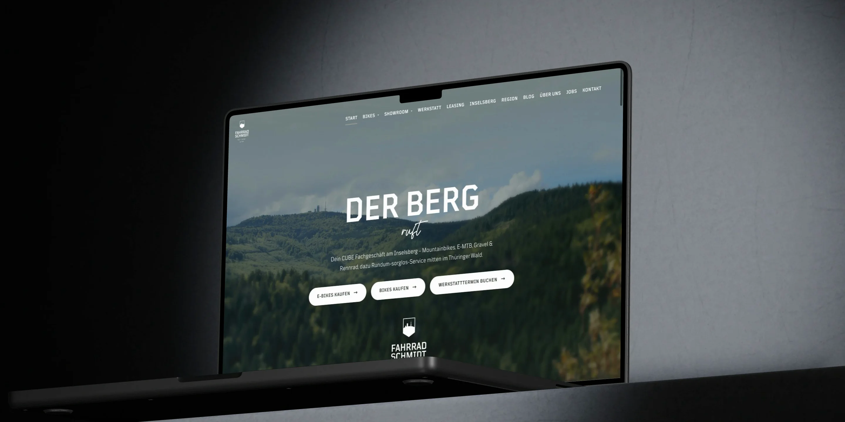 Ein MacBook Pro steht aufgeklappt in einem dunklen Raum und zeigt die Startseite von fahrrad-schmidt.de mit dem Titel Der Berg ruft über dem Inselsberg.