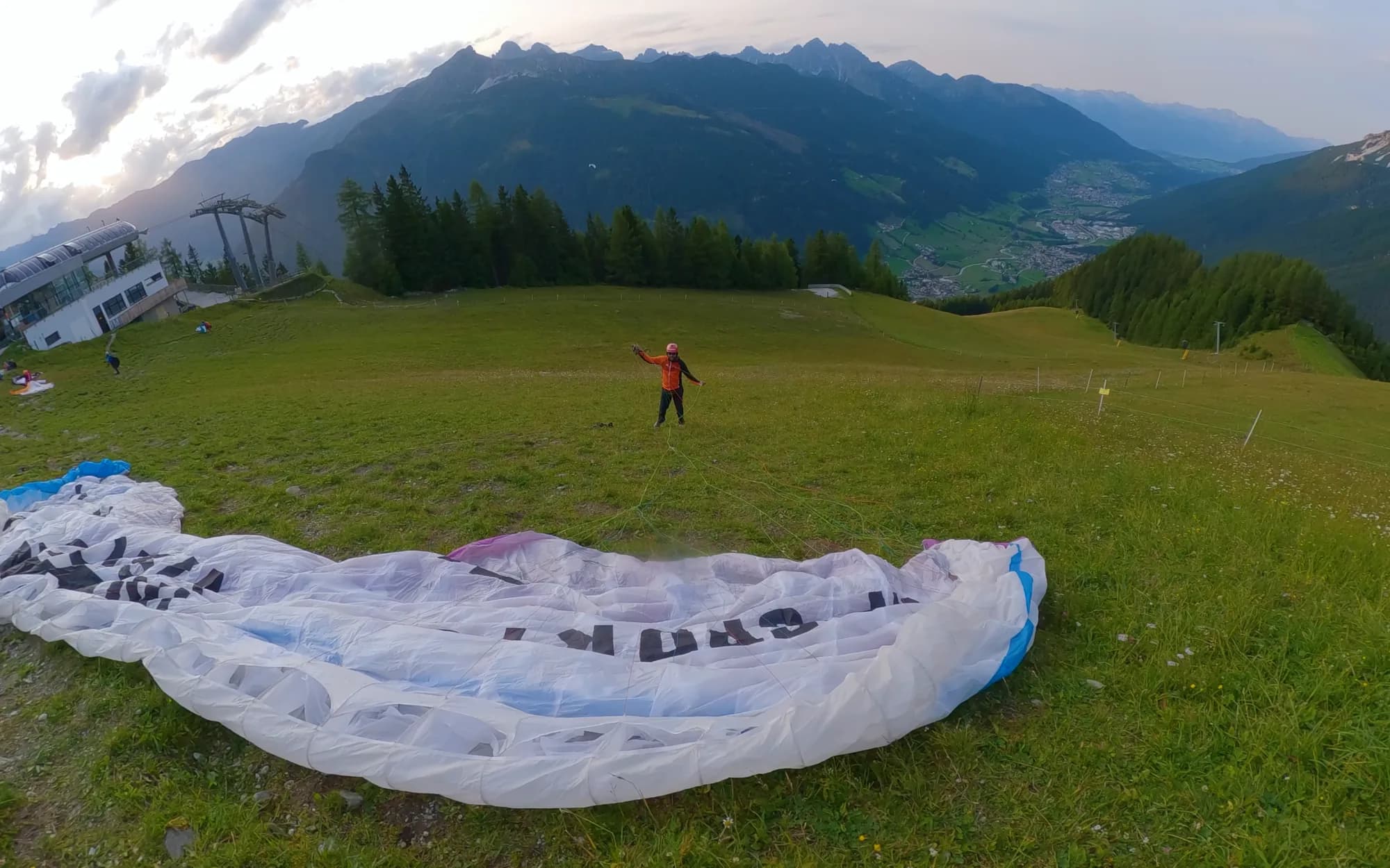 Der ausgelegte Gleitschirm auf der Startwiese über Neustift, der Pilot sortiert die Leinen, dahinter das Stubaital im Abendlicht.