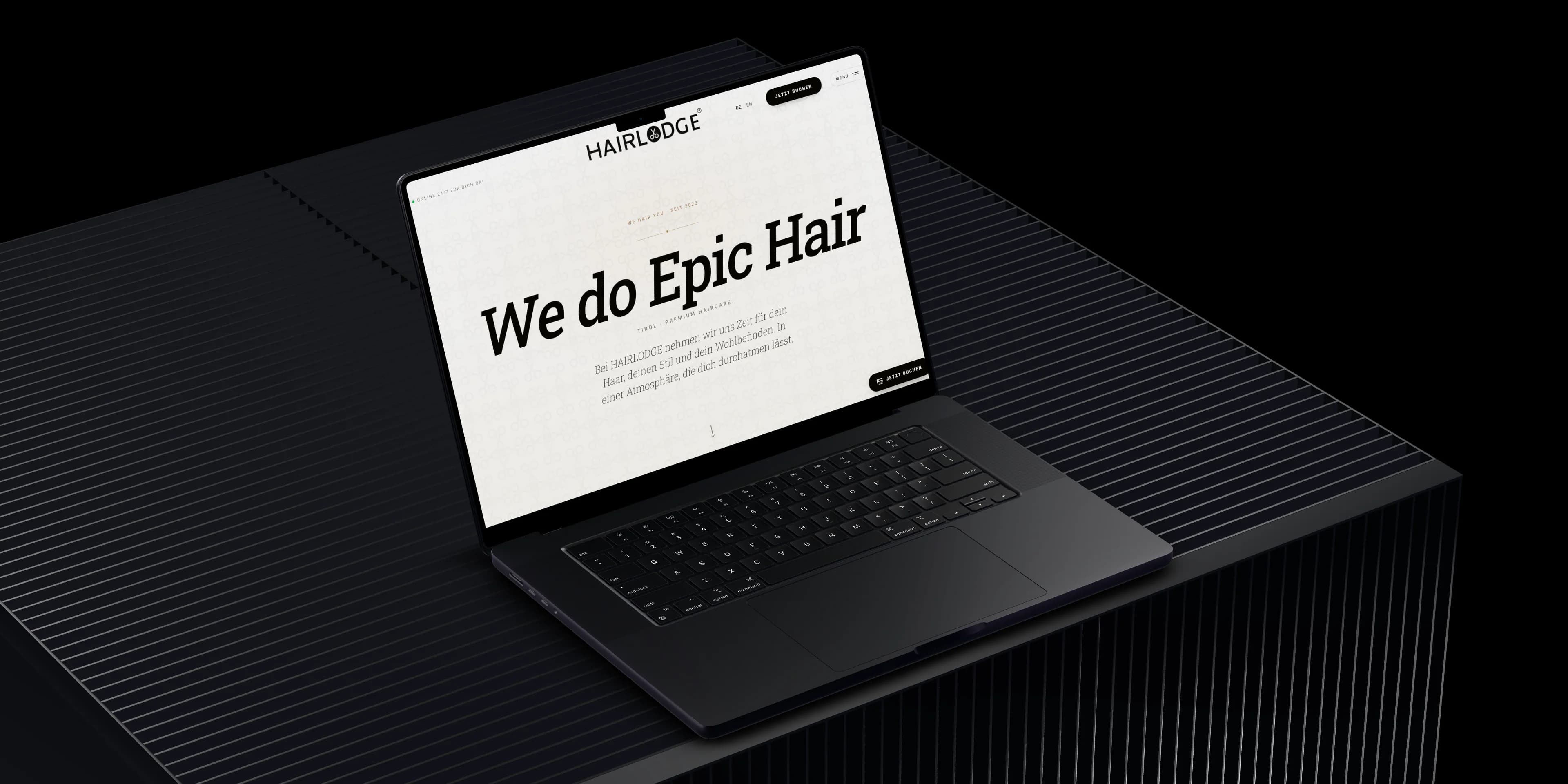 Ein MacBook Pro auf einem dunklen, gerippten Sockel zeigt die Startseite von hairlodge.at mit dem Schriftzug We do Epic Hair.