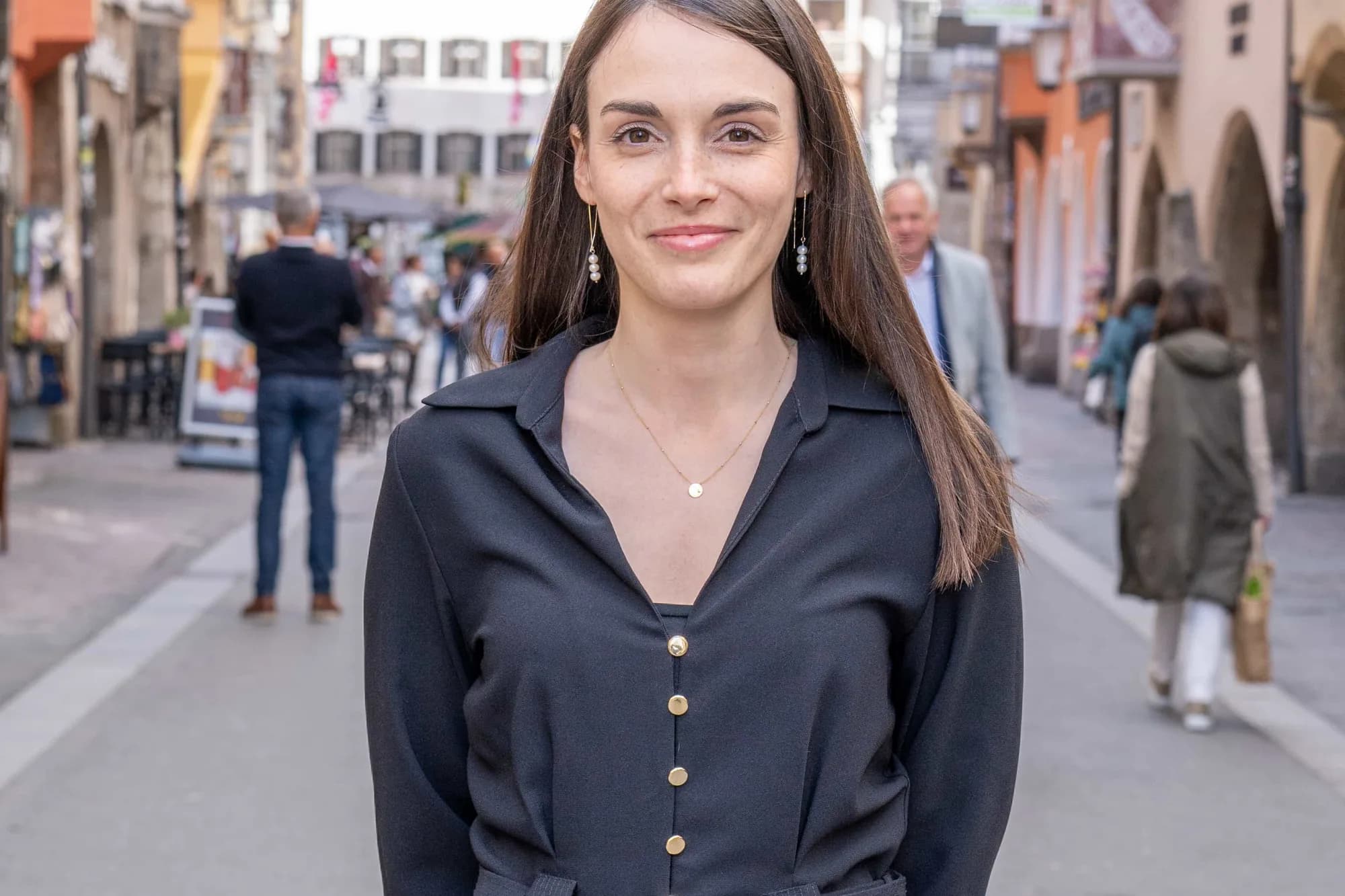 Einzelporträt in der Altstadt: eine Frau im dunklen Kleid steht in der Gasse, im Hintergrund die Arkaden und einzelne Passanten in Unschärfe.
