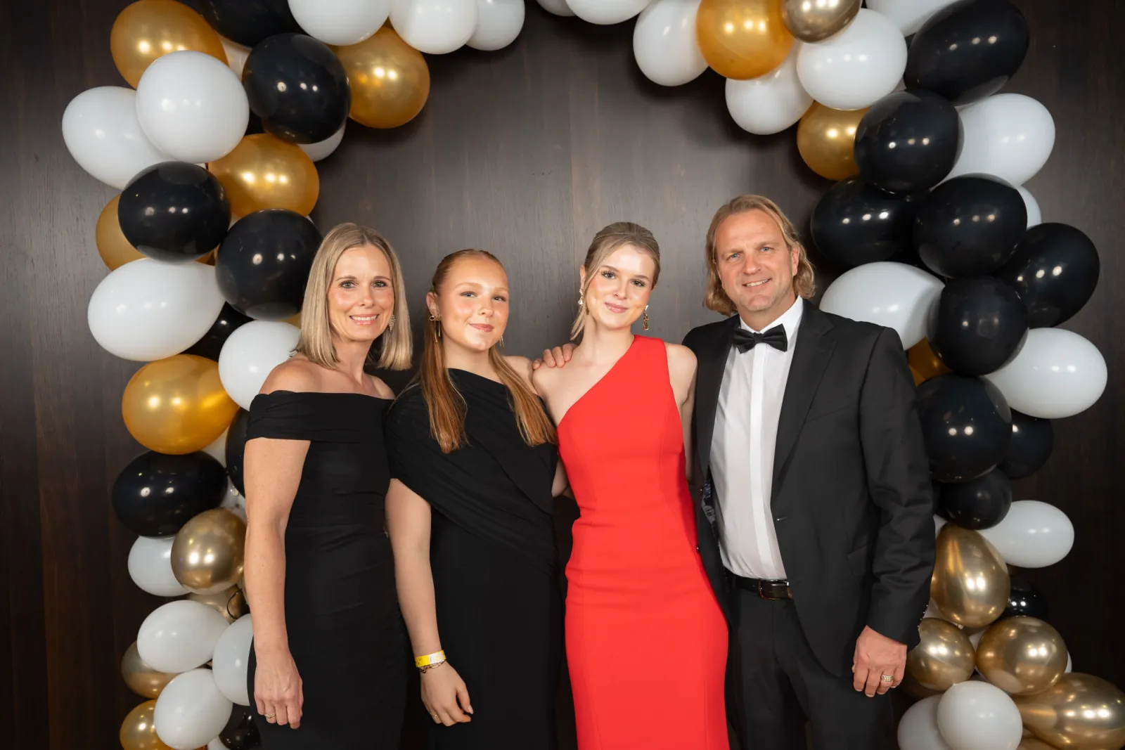 Drei Frauen in Schwarz und Rot und ein Mann im Smoking vor dem Ballonbogen