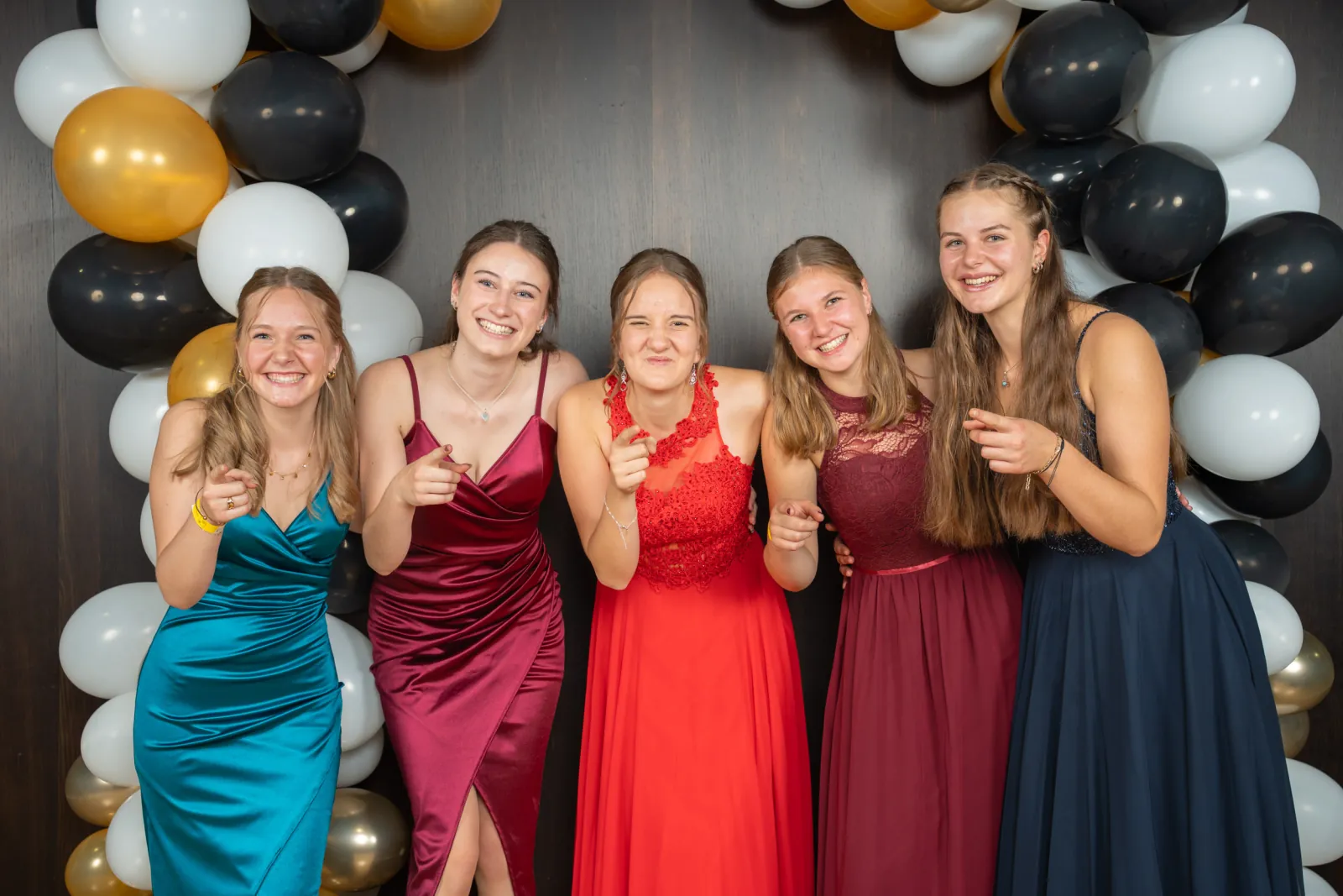 Fünf junge Frauen in Rot, Petrol und Bordeaux zeigen in die Kamera