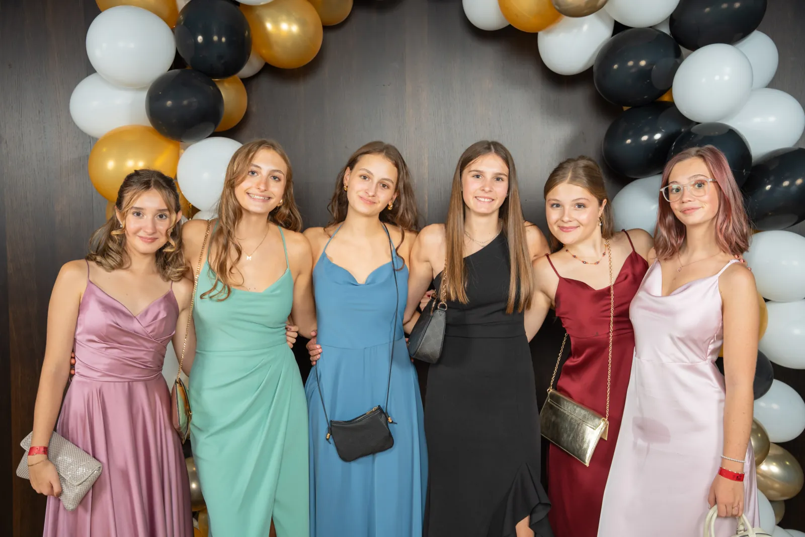 Sechs junge Frauen in Pastellkleidern aufgereiht vor dem Ballonbogen