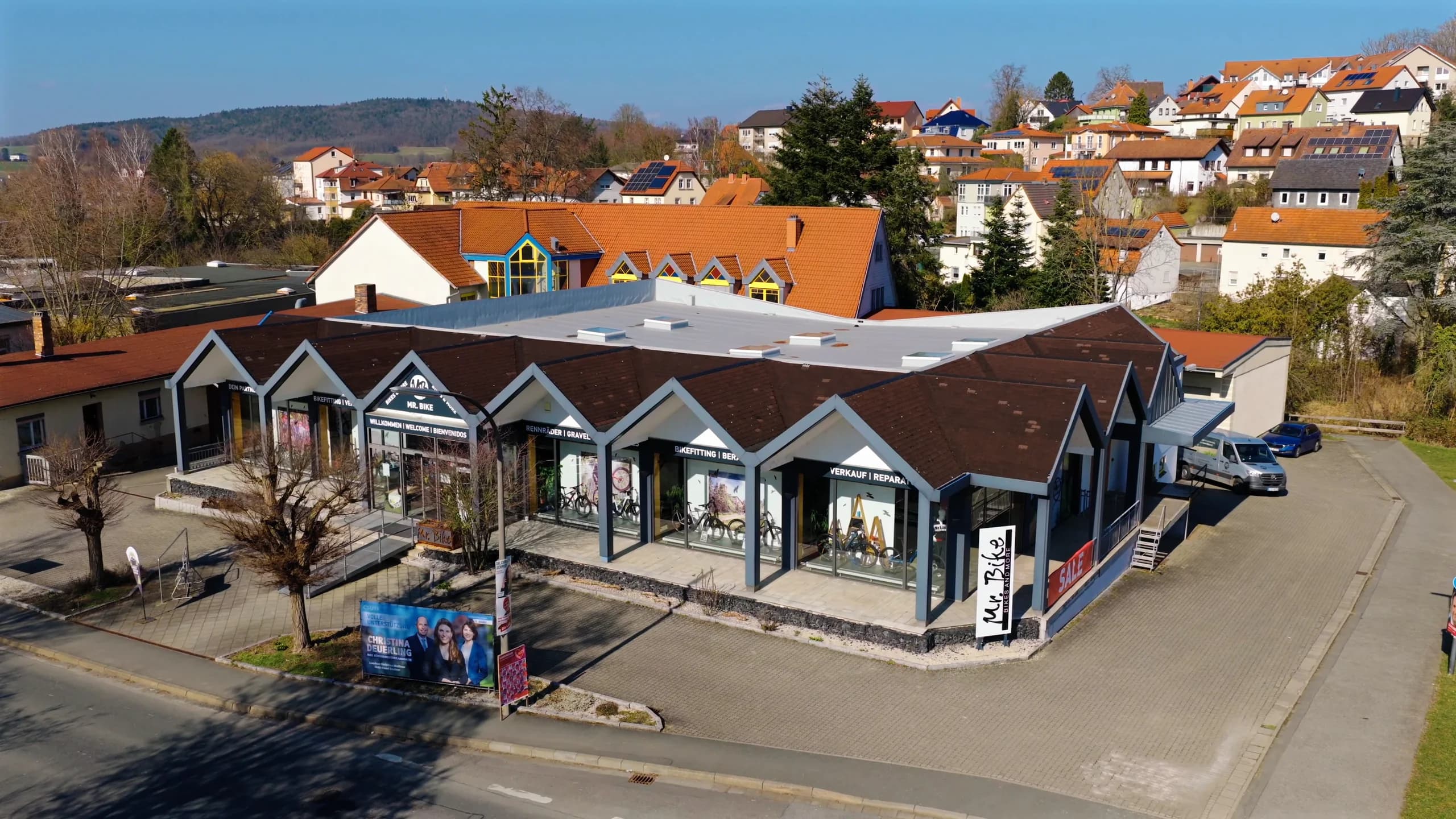 Der Mr. Bike Store in Lichtenfels aus der Luft: die Giebelreihe mit den Schaufenstern, davor die Strasse mit der Mr.-Bike-Fahne, dahinter die Dächer des Orts.