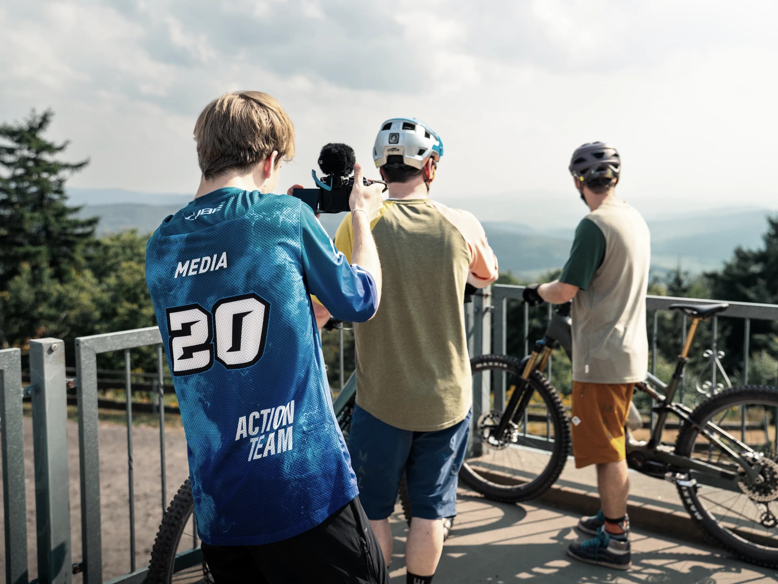 Videograf der Werbeagentur Invisions filmt zwei Mountainbiker auf einer Aussichtsplattform, dahinter die Hügelkette.