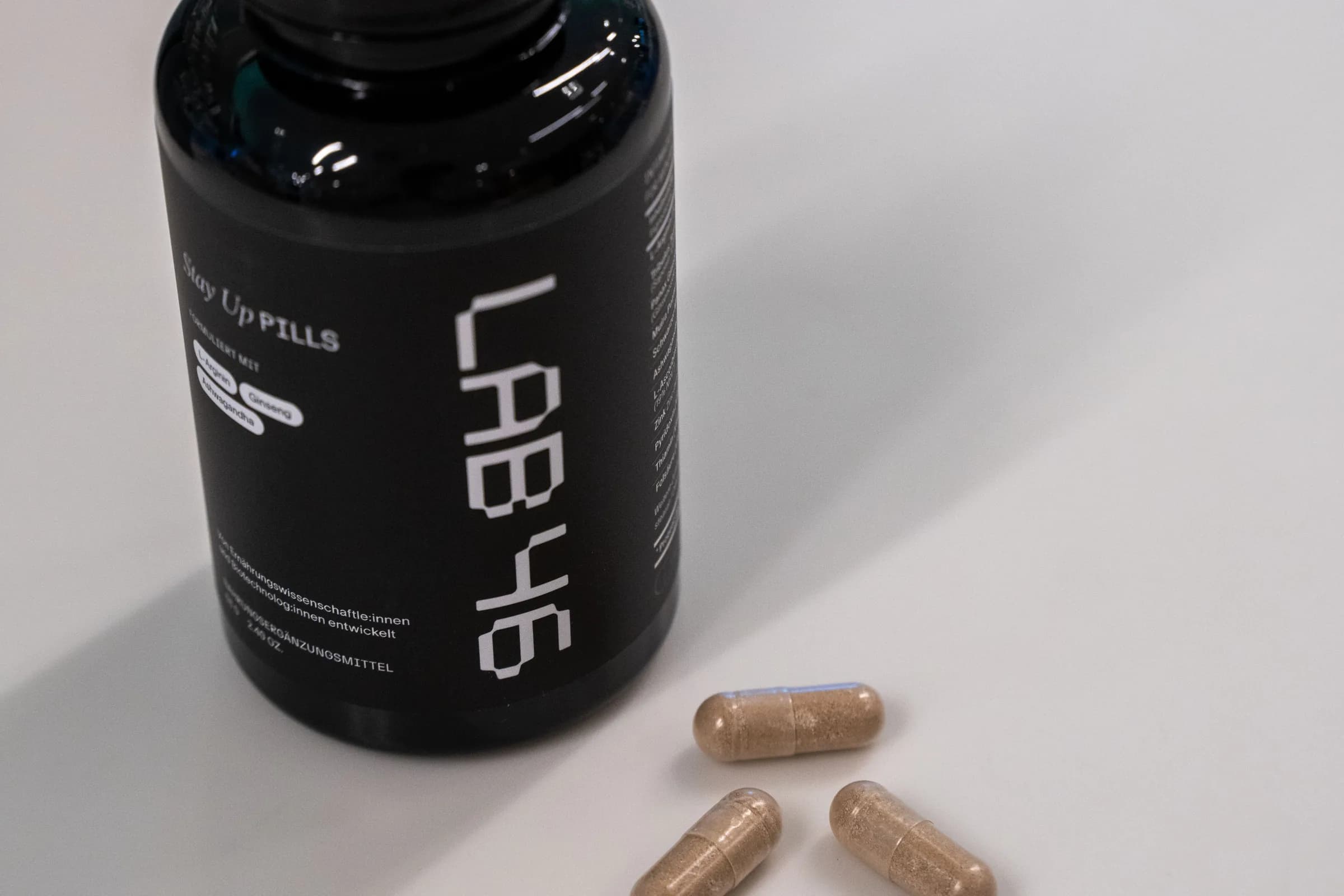 Eine schwarze LAB46-Dose steht auf der weissen Theke, davor liegen drei Kapseln.