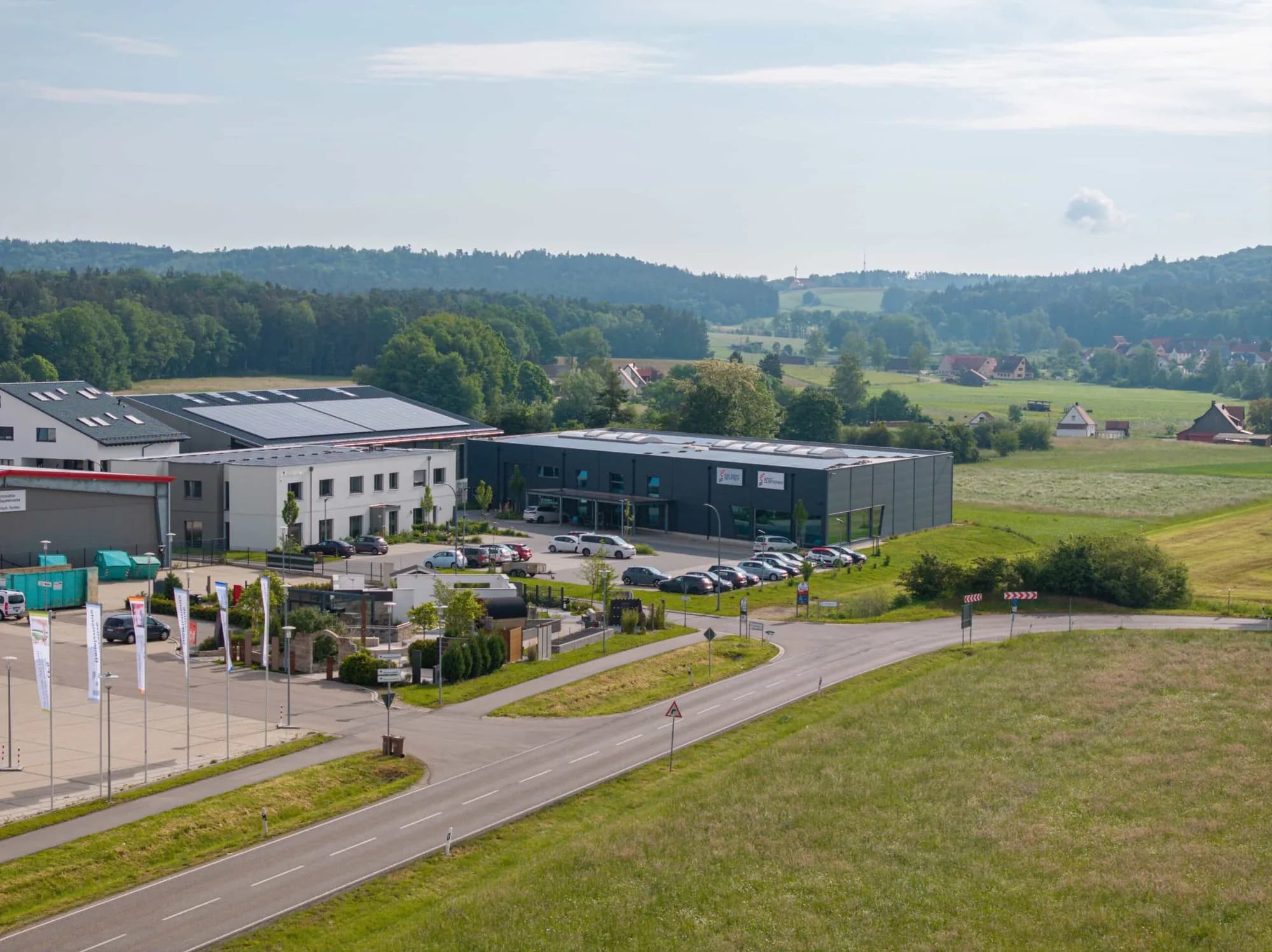 Das Geschäftsgebäude von Rad Sport Schmidt aus der Luft: die dunkle Halle mit Parkplatz davor, dahinter Felder, Wald und die Häuser am Ortsrand.