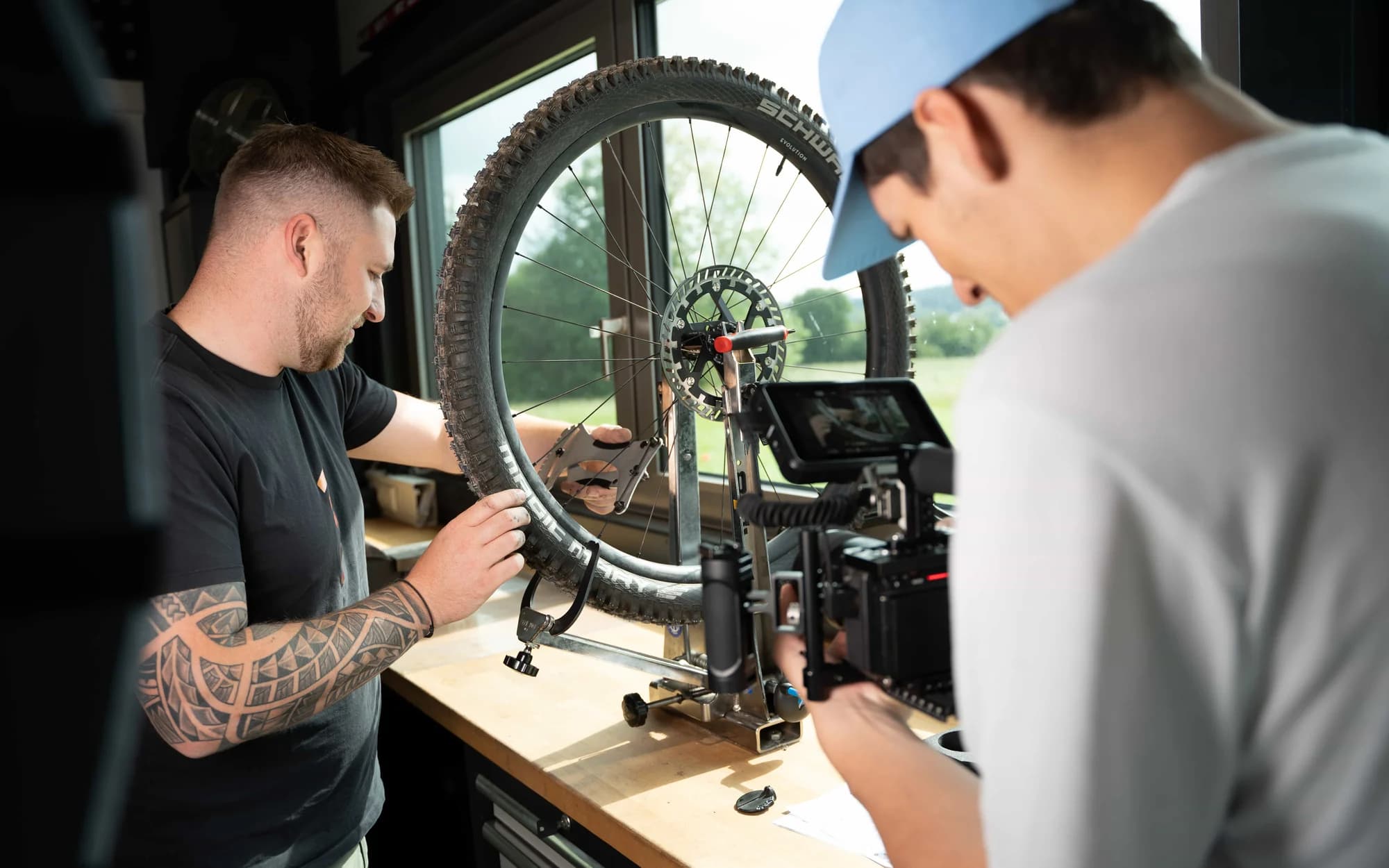 In der Werkstatt hält ein Mechaniker ein Laufrad in den Ständer, daneben filmt jemand die Szene mit einer Kamera auf einem Slider.