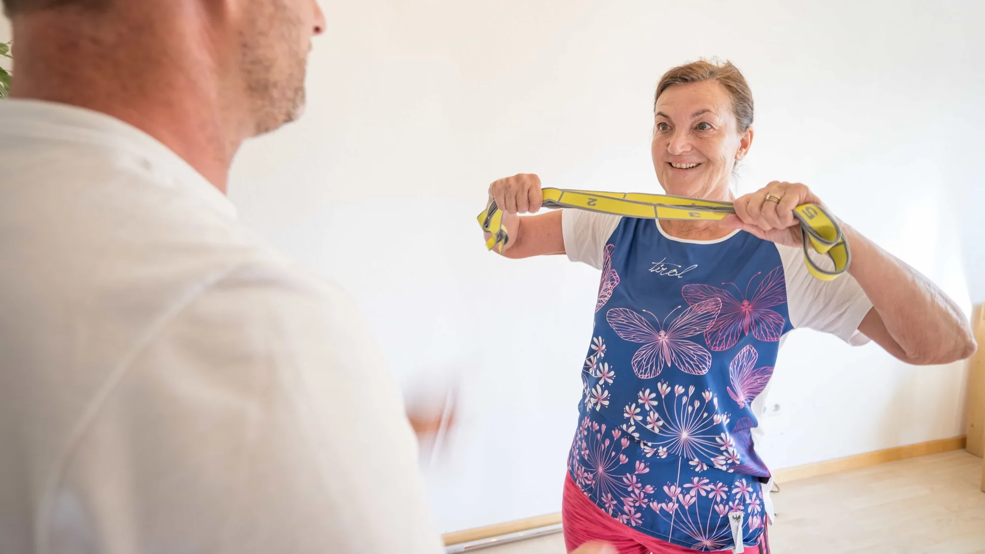 Eine Kundin zieht lächelnd ein gelbes Widerstandsband auseinander, im Vordergrund unscharf die Schulter von Robert Treitinger.