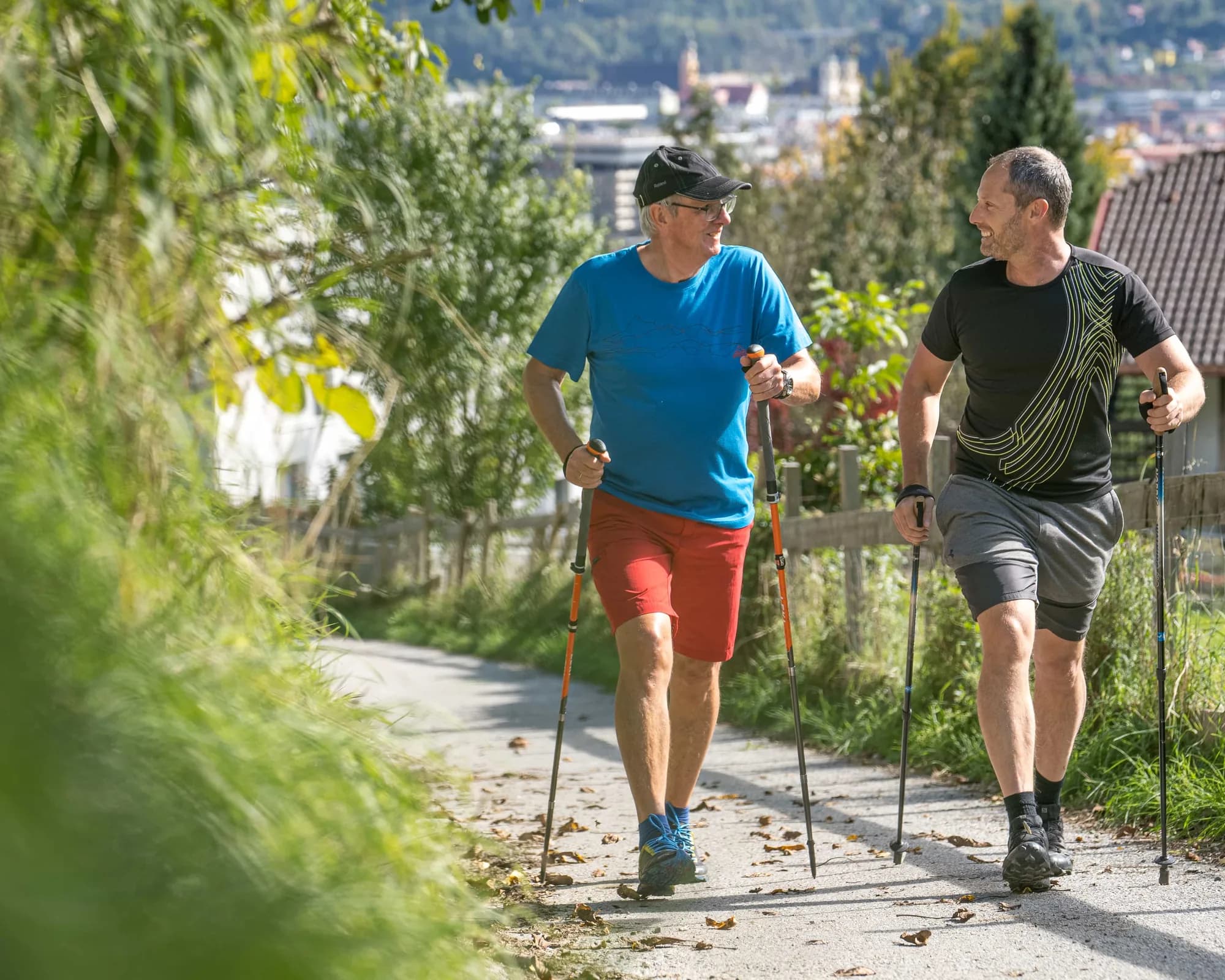 Robert Treitinger beim Walken mit einem Kunden auf einem Weg über Innsbruck, beide mit Stöcken, die Stadt und die Berge dahinter.