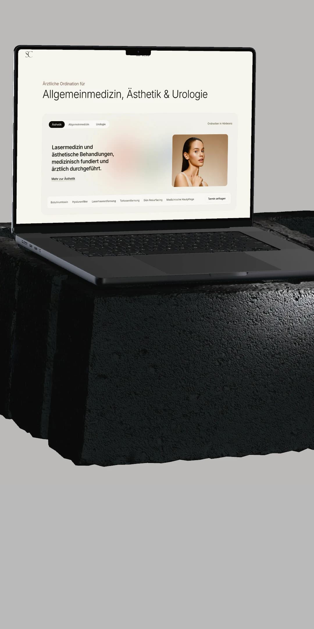 Ein MacBook auf einem dunklen Steinsockel vor hellgrauem Grund zeigt die Startseite von skinchic.at mit den drei Fachbereichen.