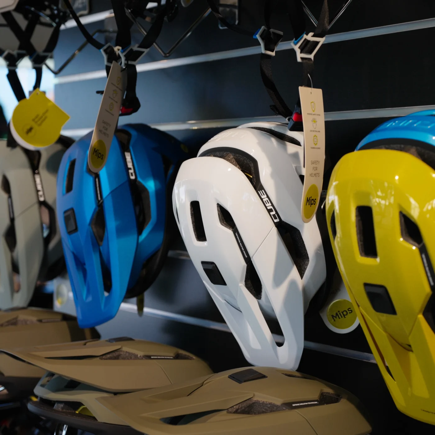 Fahrradhelme in Blau, Weiss und Gelb hängen in einer Reihe an der Wand, darunter Sättel.