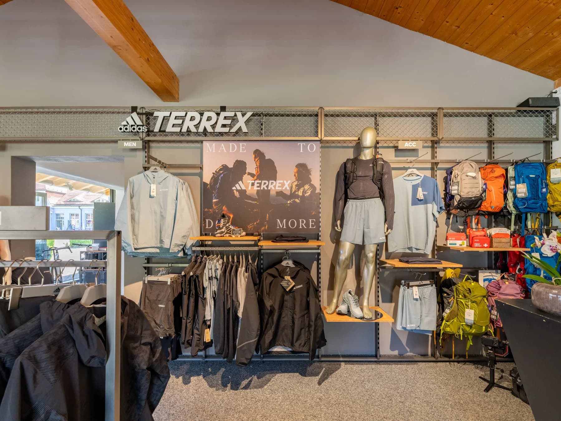 Die Bekleidungsabteilung mit Terrex-Schriftzug, Jacken auf Stangen und Rucksäcken im Regal.