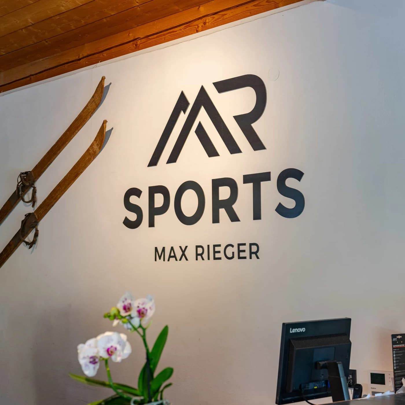 Der Schriftzug MR Sports Max Rieger auf einer hellen Wand, daneben zwei alte Holzskier.