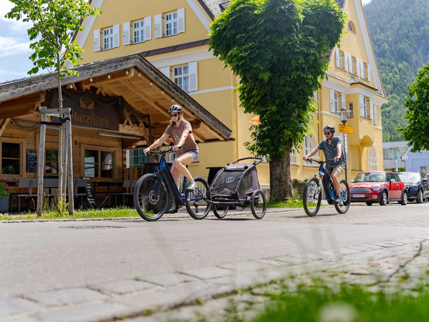 Eine Radfahrerin mit Kinderanhänger auf der Dorfstrasse in Mittenwald, dahinter die bemalten Häuser.